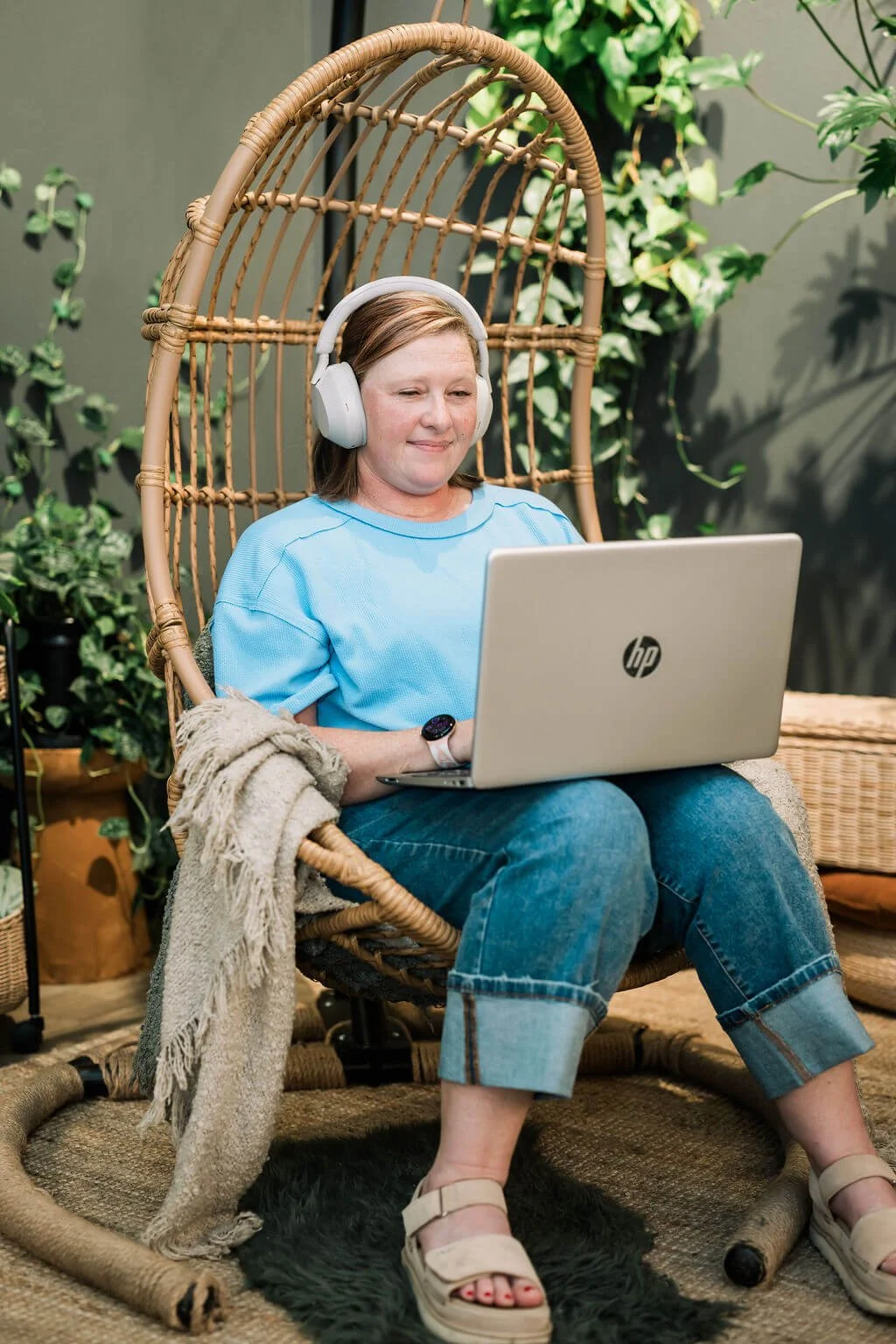 Liz Chapman is sitting in a hanging basket chair with her laptop in her lap and headphones on her head