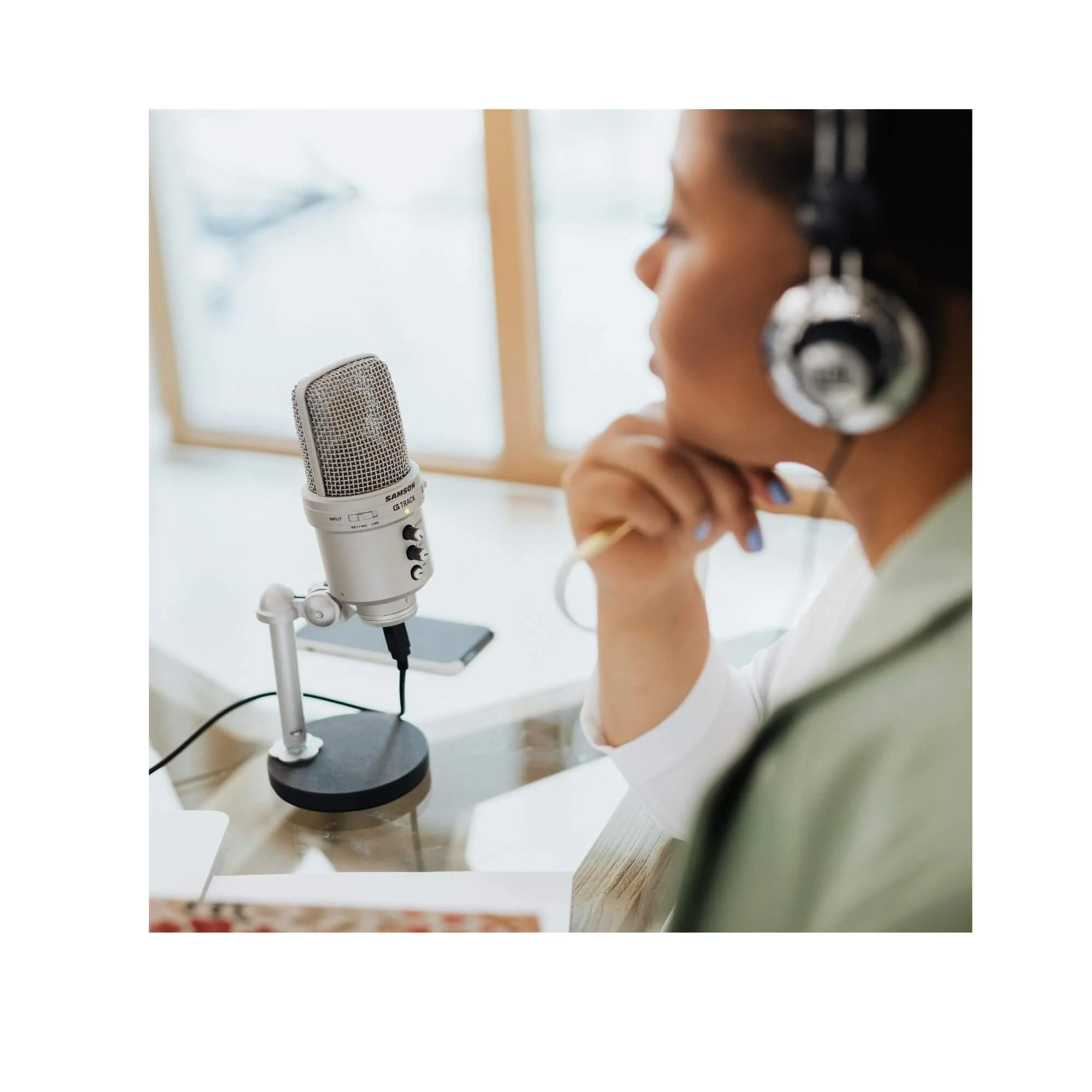 Image is of a person looking pensively at their microphone with their hand under their chin and wearing headphones