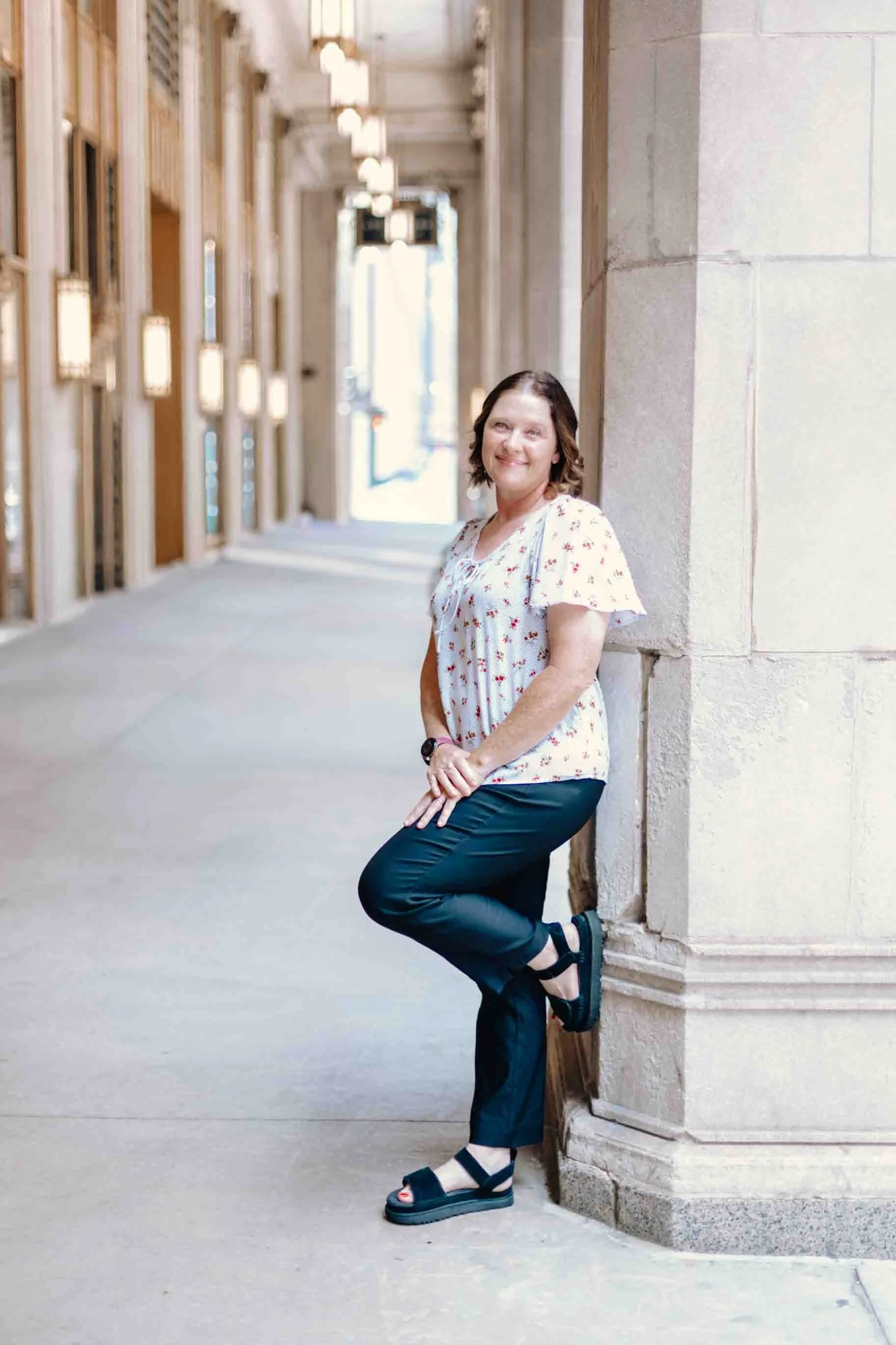 Liz Chapman, podcast launch specialist, strategist and manager smiling at the camera with her left foot up on the pillar that she is leaning against in downtown Chicago