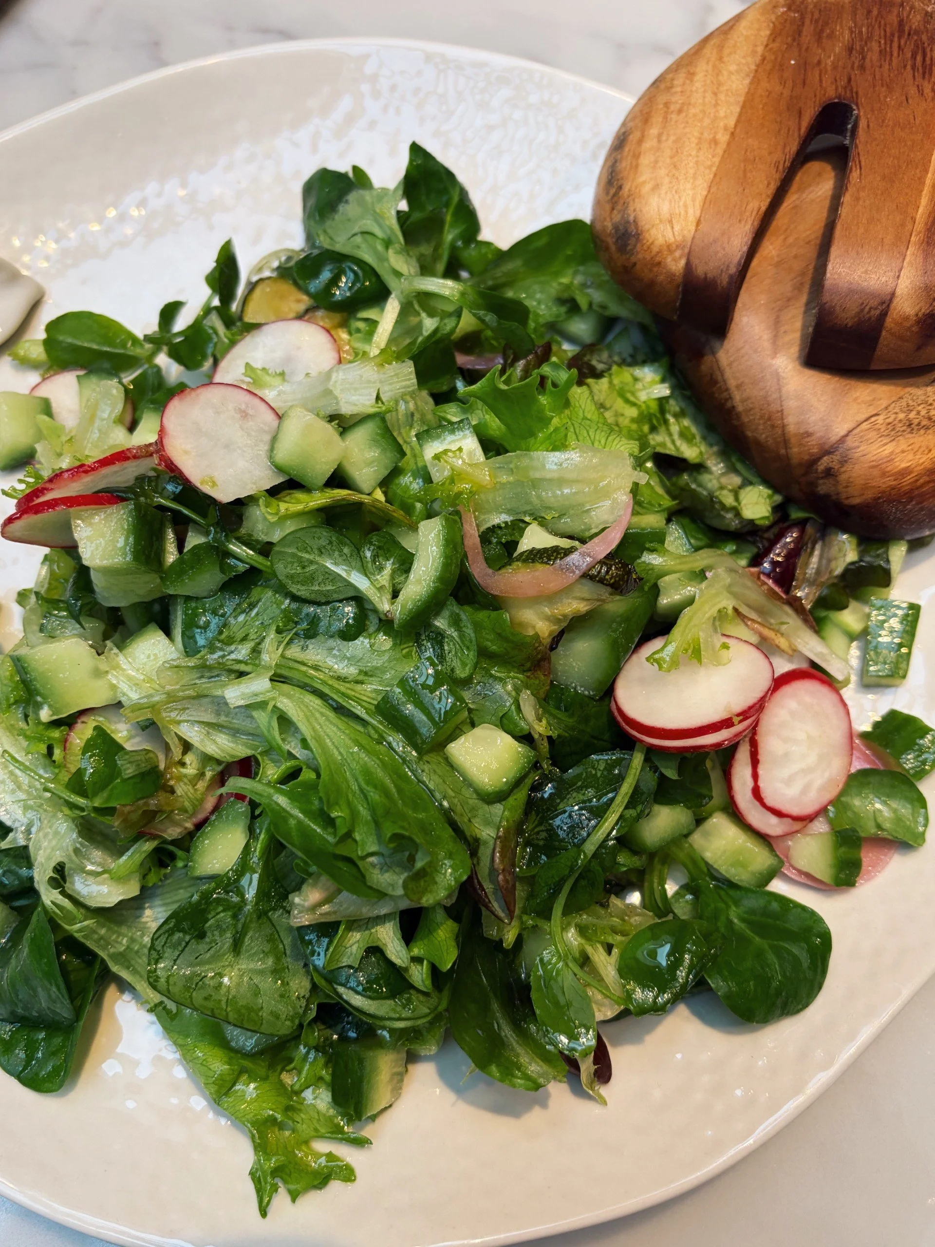 French bisto salad with radishes and cucumbers on a white plate, with a wooden salad serving utensil.