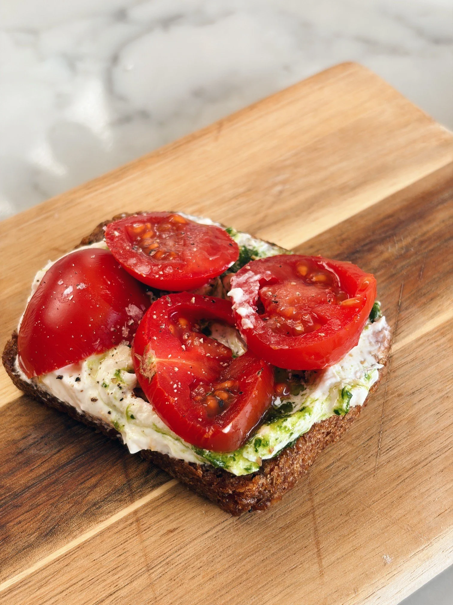 Smørrebrød topped with whipped goat's cheese, lemon, pepper, tomatoes and fresh parsley oil. 