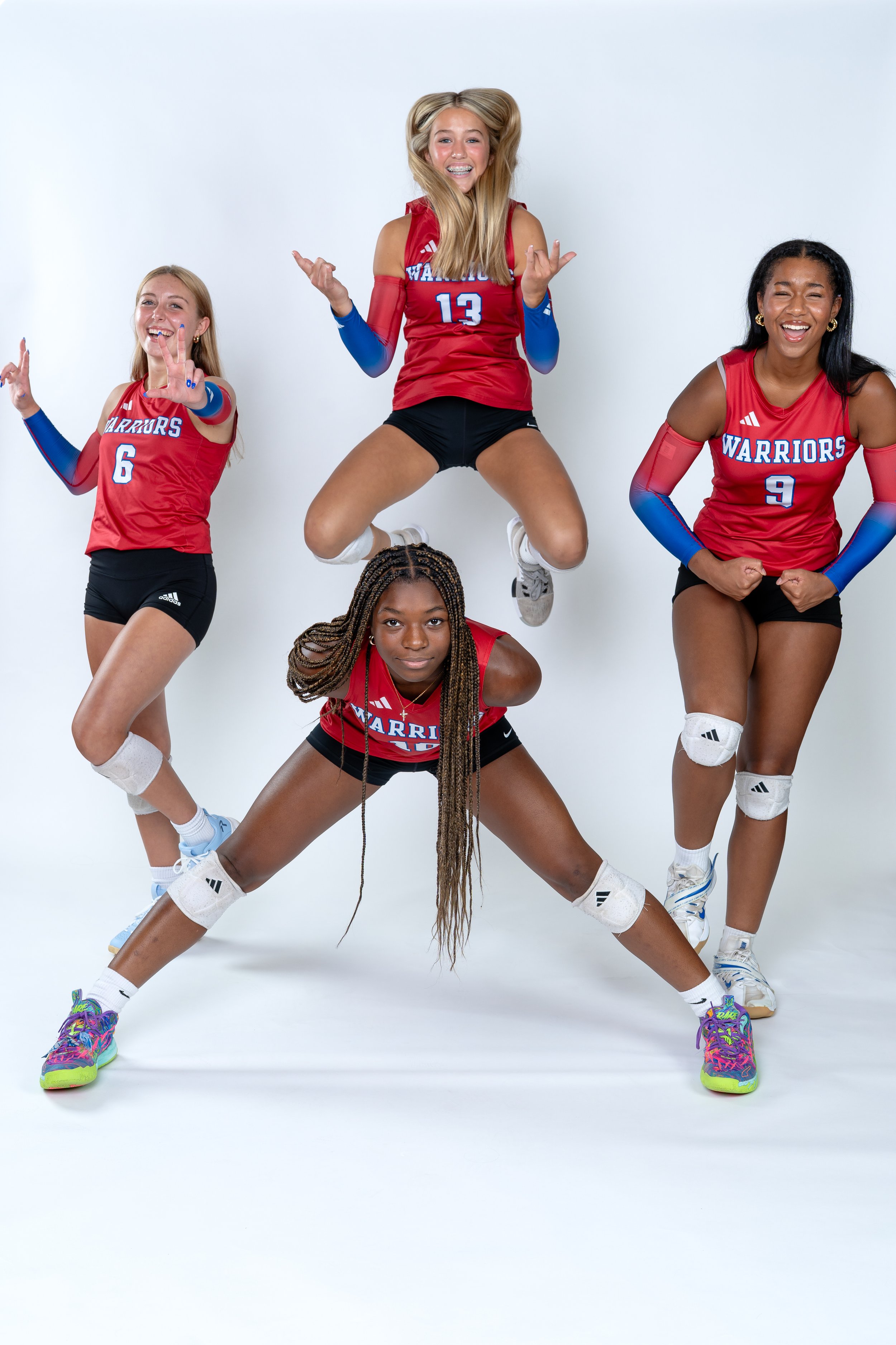 Four young female volleyball players in red team uniforms posing and jumping, with some making peace signs and excited expressions.