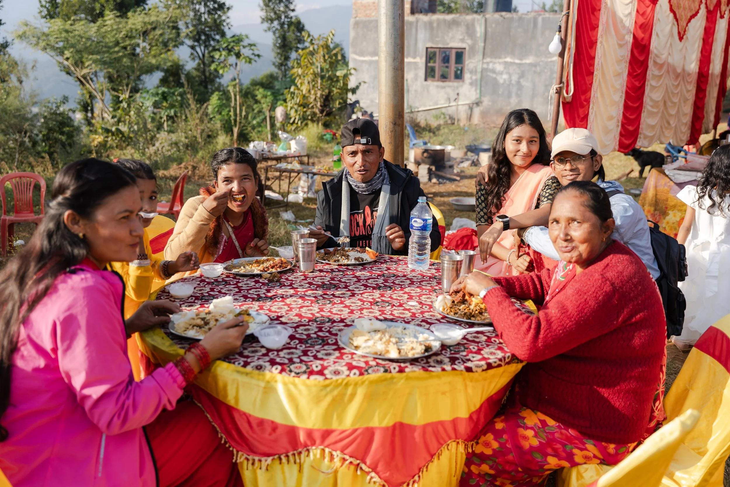 Group of people enjoying a meal outdoors at a festive gathering with colorful decorations.