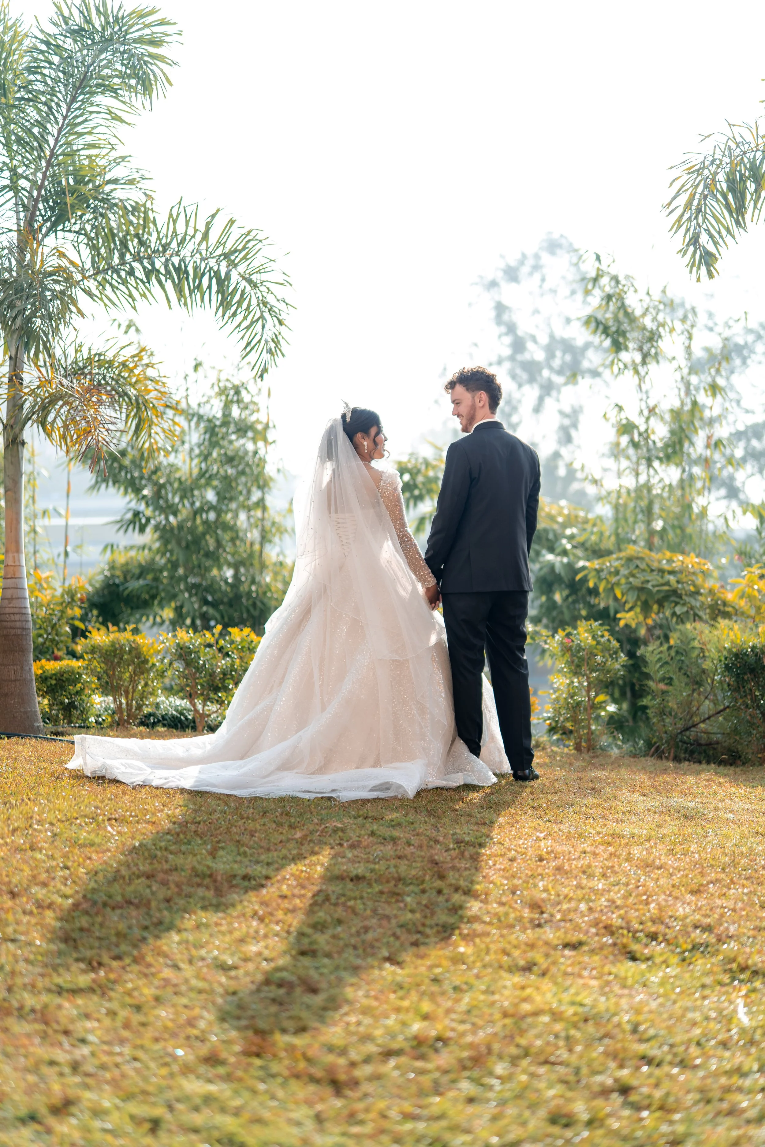 A bride and groom holding hands outside among greenery and palm trees on their wedding day.