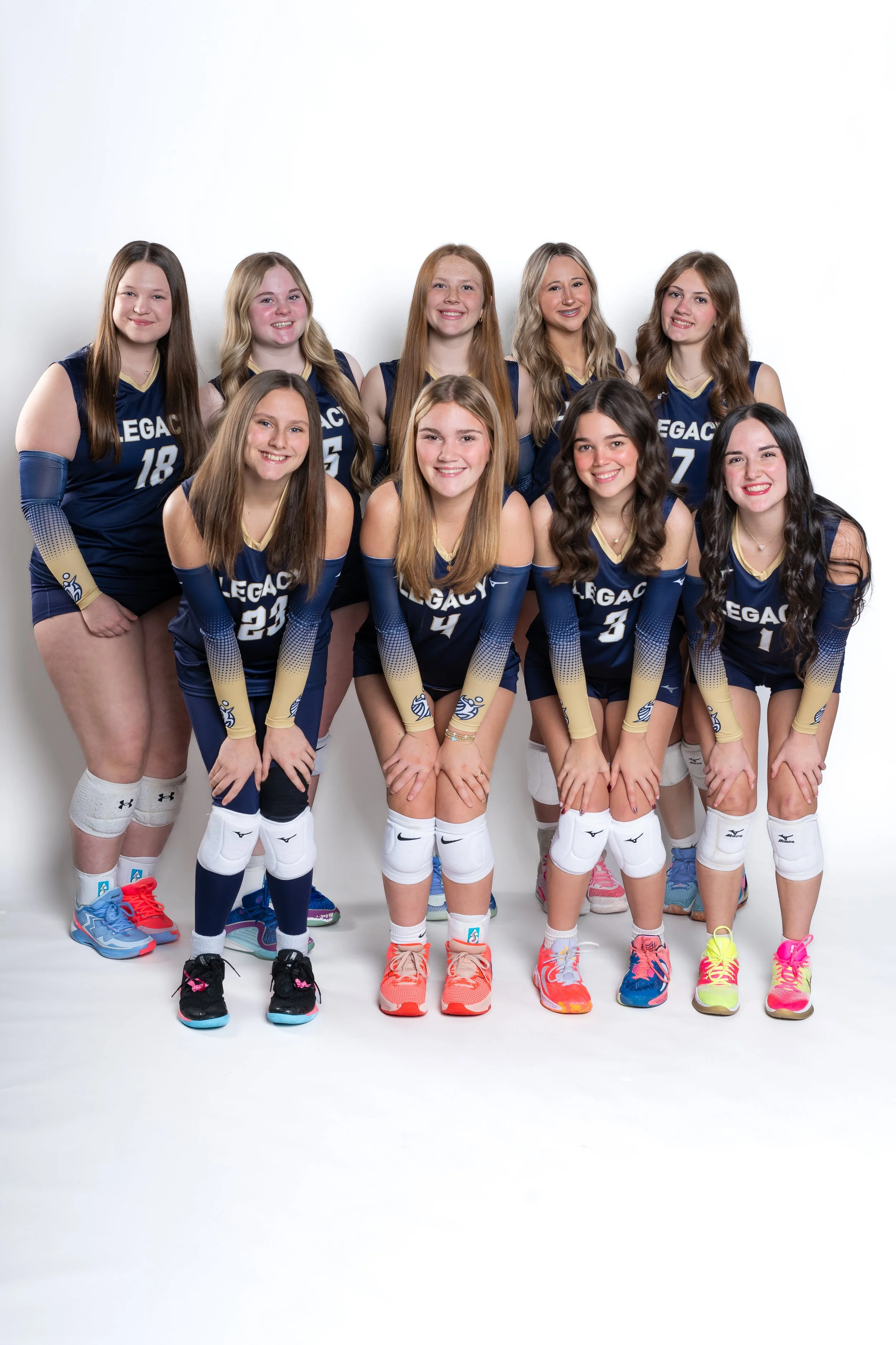 Group of ten female volleyball players in navy and gold uniforms posing together in studio.