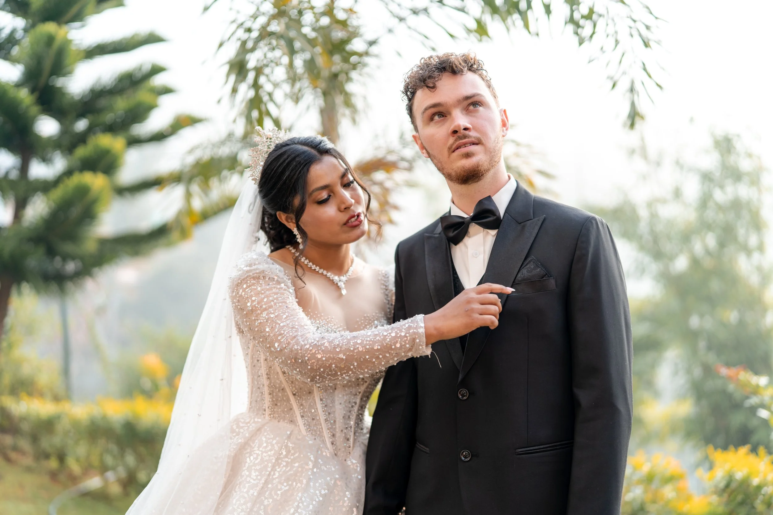 Bride adjusting groom's tuxedo in an outdoor garden setting.