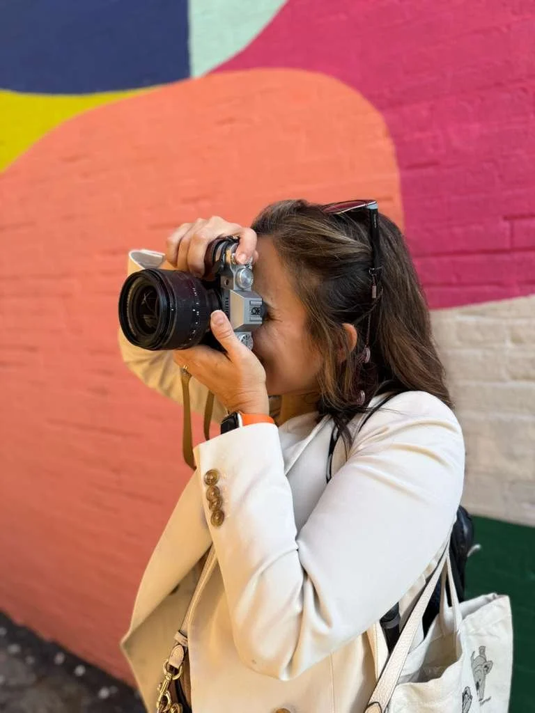 Woman taking a photograph with a camera in front of a colorful abstract mural.