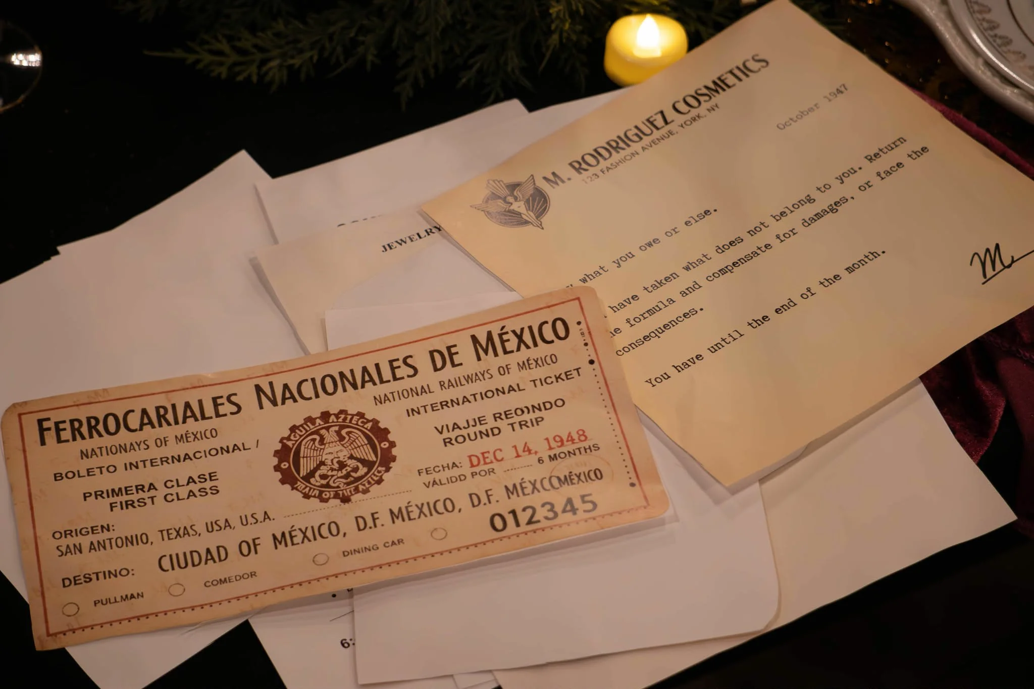 Vintage Mexican train ticket, a letter from M. Rodriguez Cosmetics, and a diamond-shaped white envelope on a dark table with a candle.