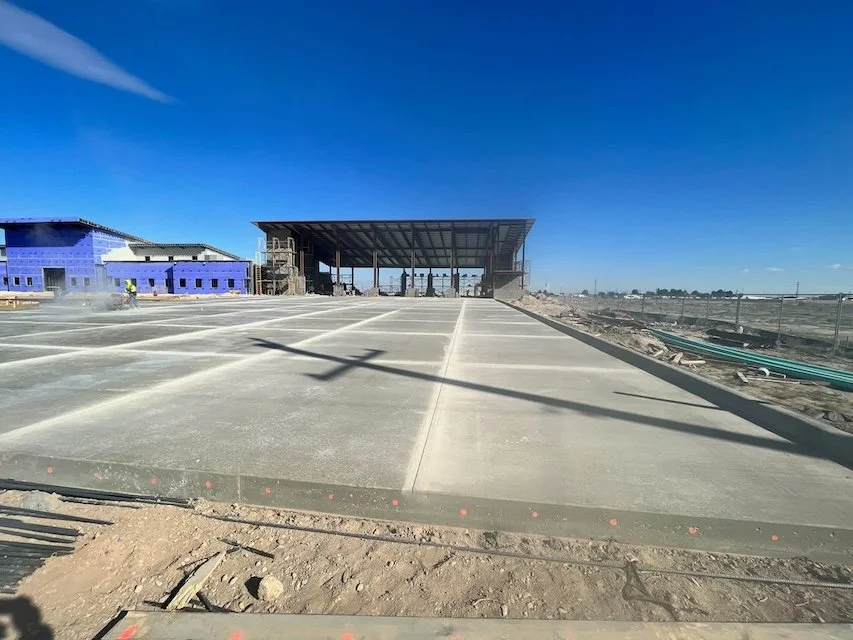Construction site with a new building under construction, concrete pavement, and a clear blue sky.