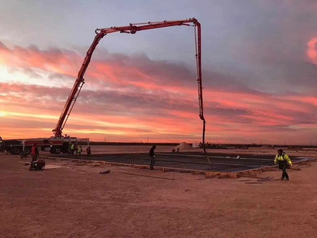 Construction workers pouring concrete on a foundation at sunset, using a concrete pump truck with an extendable arm.