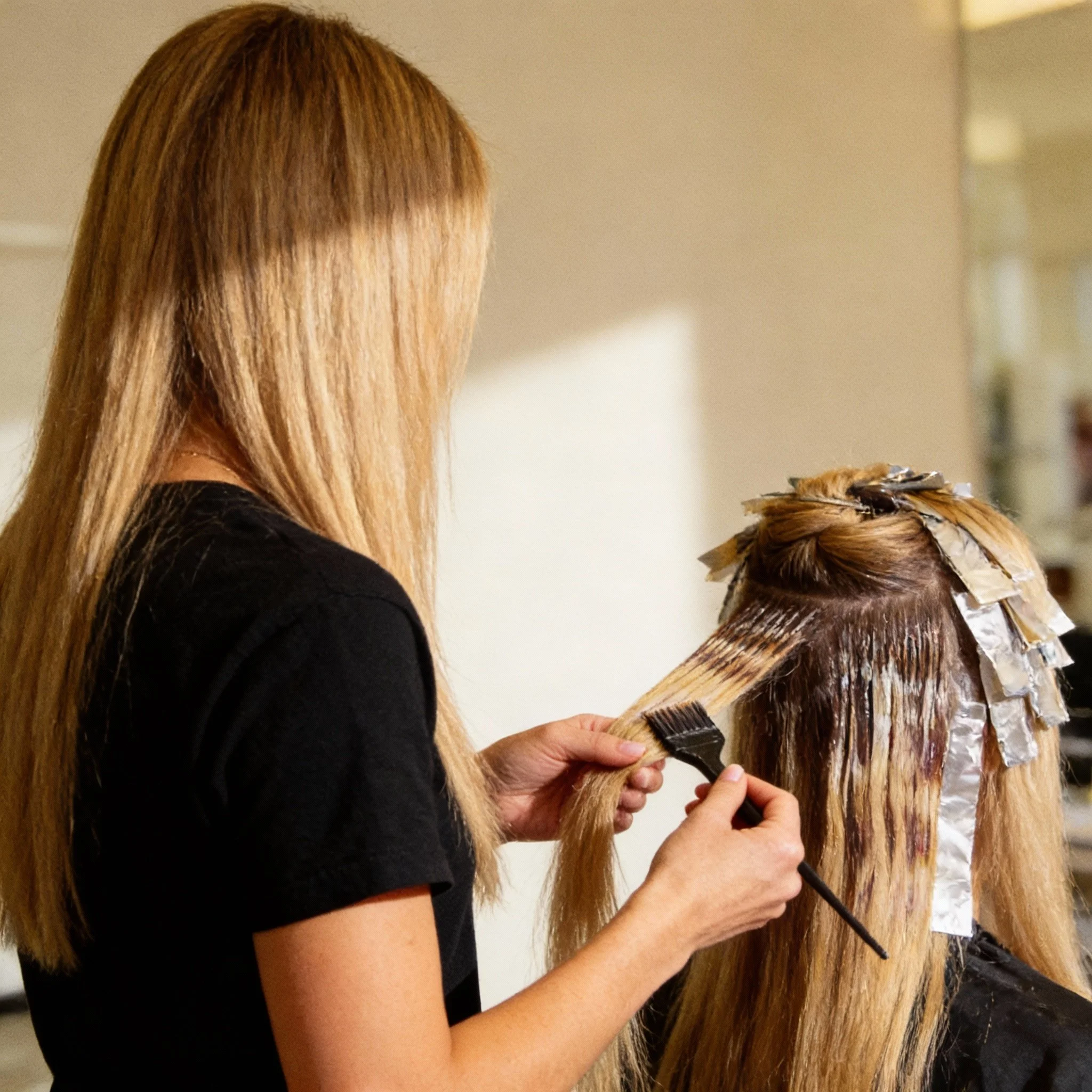 Een kapster verft een vrouw haar haar met folie en borstel in een salon van Élure Hair Clinic..