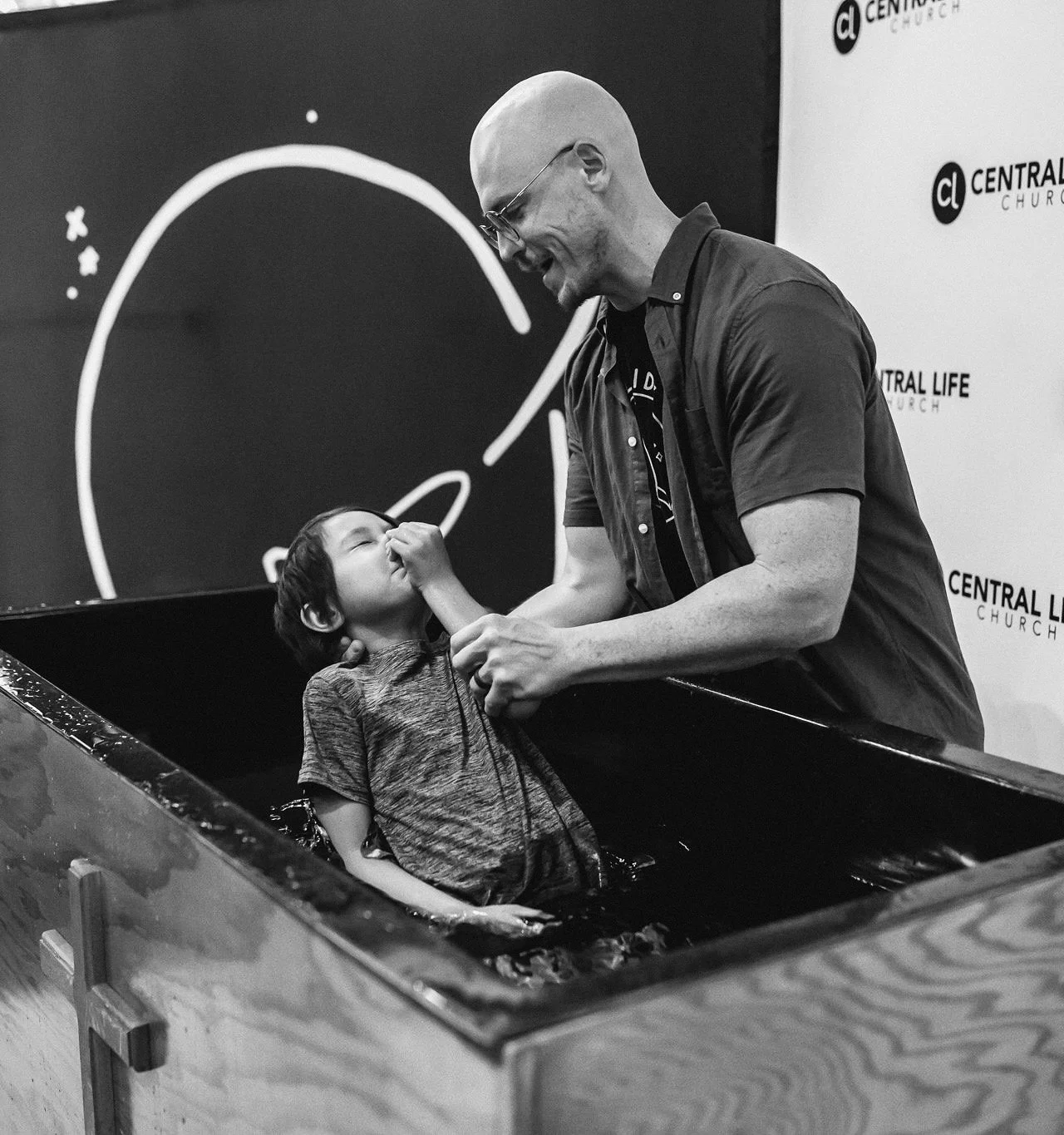 A man baptizing a young boy in a water baptism tank during a church service.