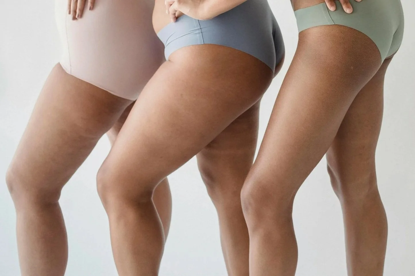 Close-up of three women in different colored underwear, focusing on their legs and hips, standing against a plain background.