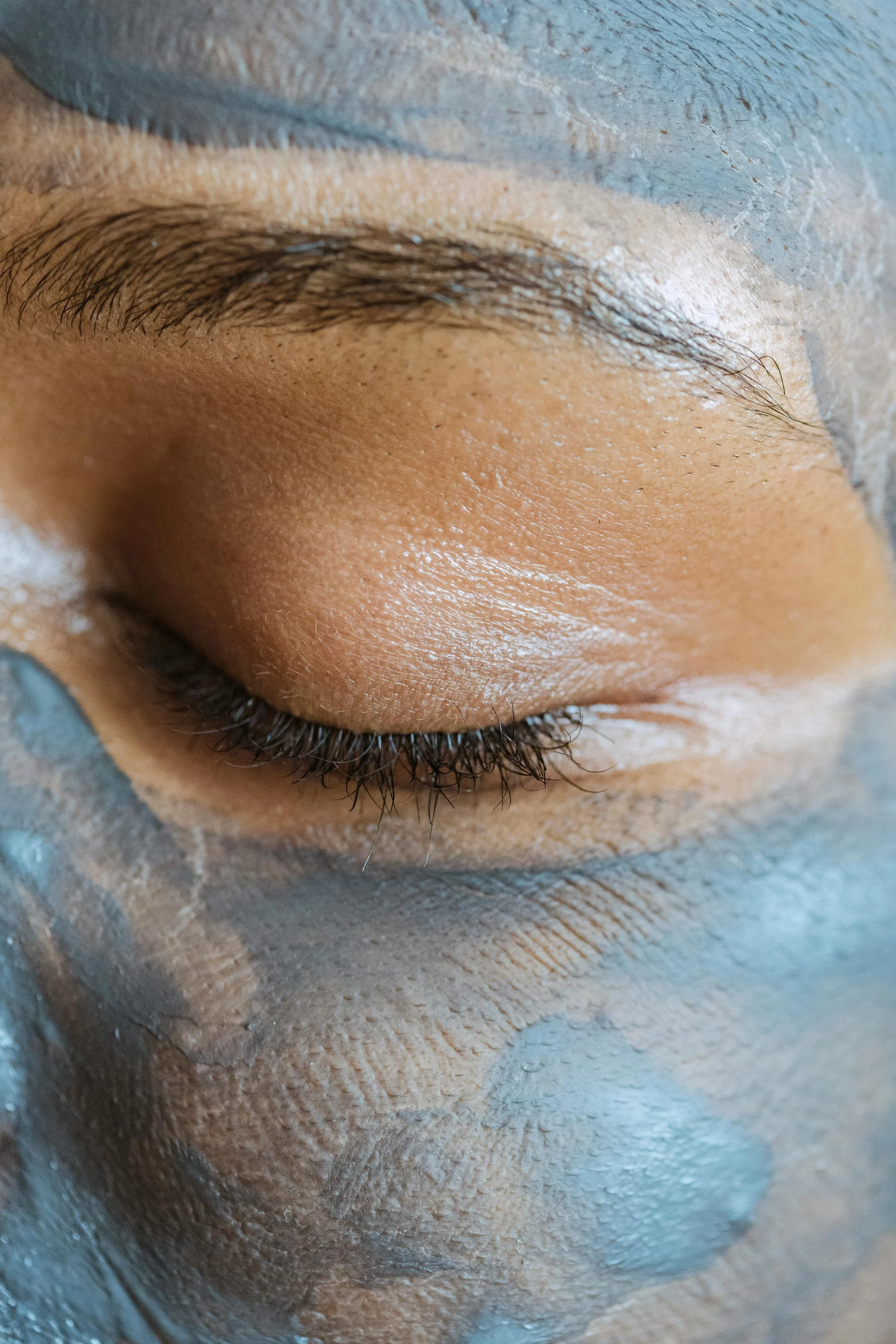 Close-up of a person's closed eye with a facial mask applied and some foam around the eye area.