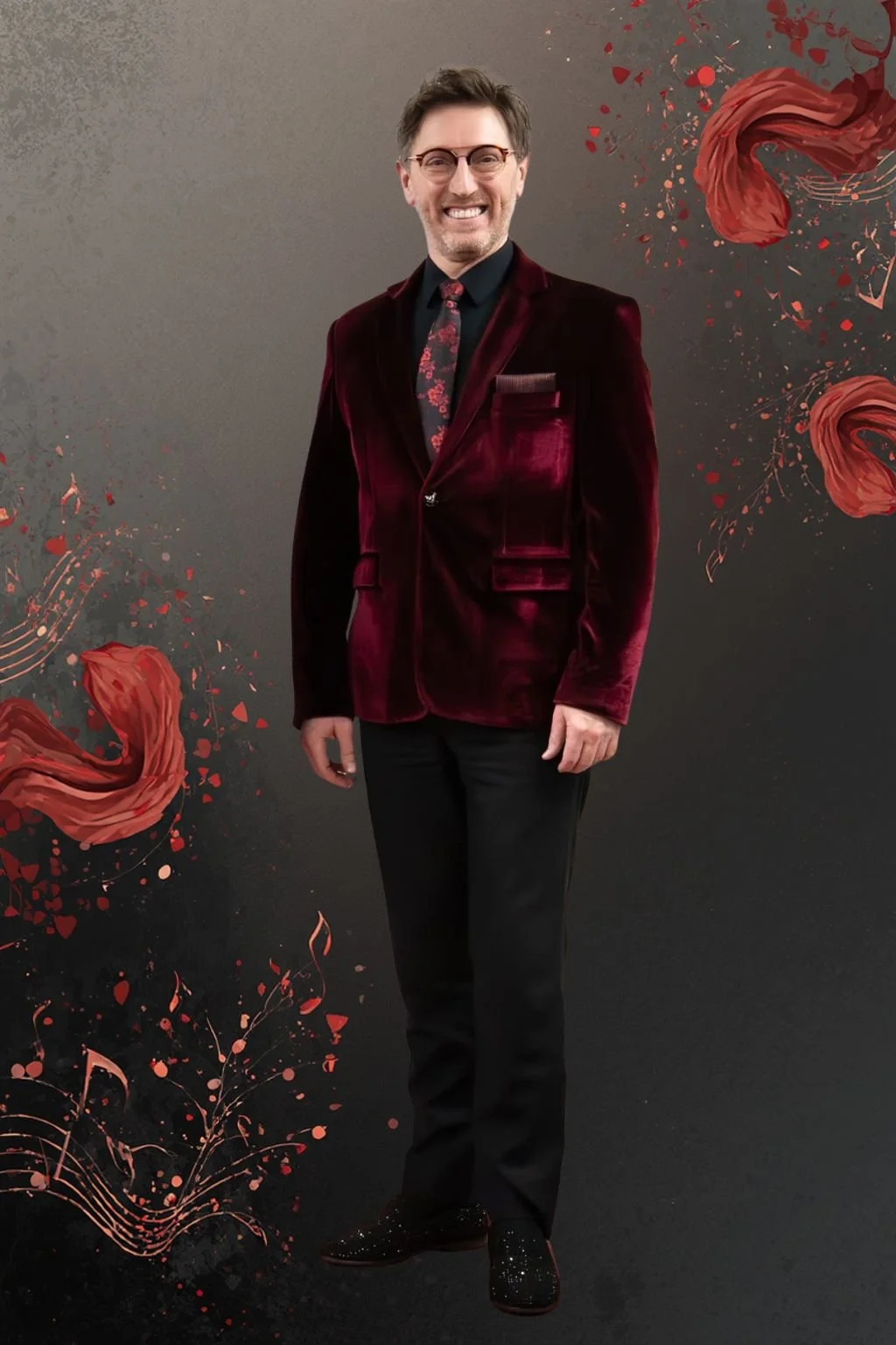 A man smiling, wearing glasses, a burgundy velvet blazer with multiple pockets, a black shirt, a floral tie, black pants, and black shoes with glitter, standing against a dark background decorated with abstract red floral designs.