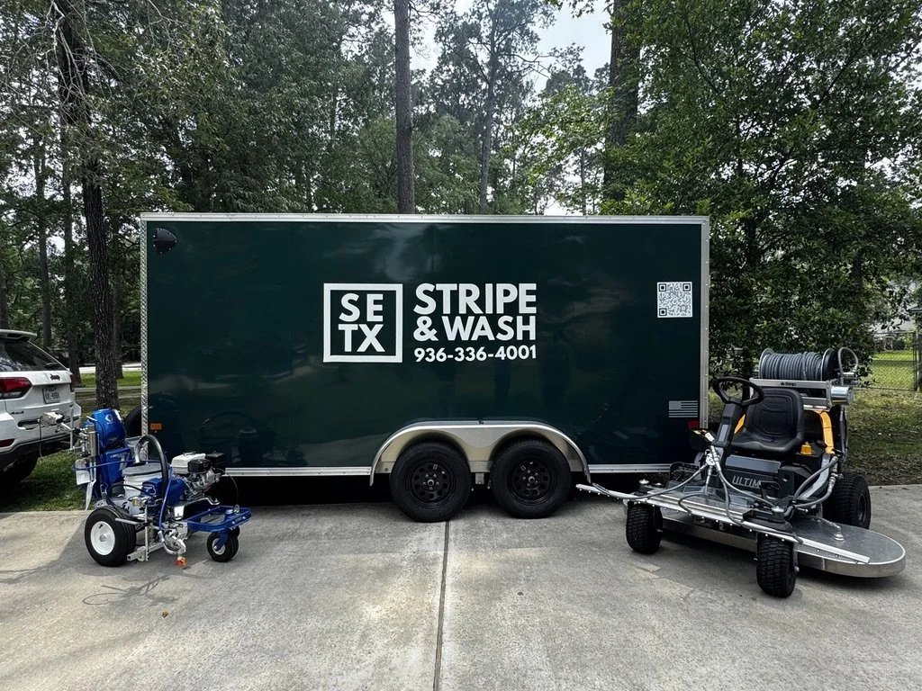 A green trailer with a large white sign reading "SE TX STRIPE & WASH" and a phone number, parked on a concrete surface outdoors, with cleaning equipment and a golf cart nearby, trees in the background.