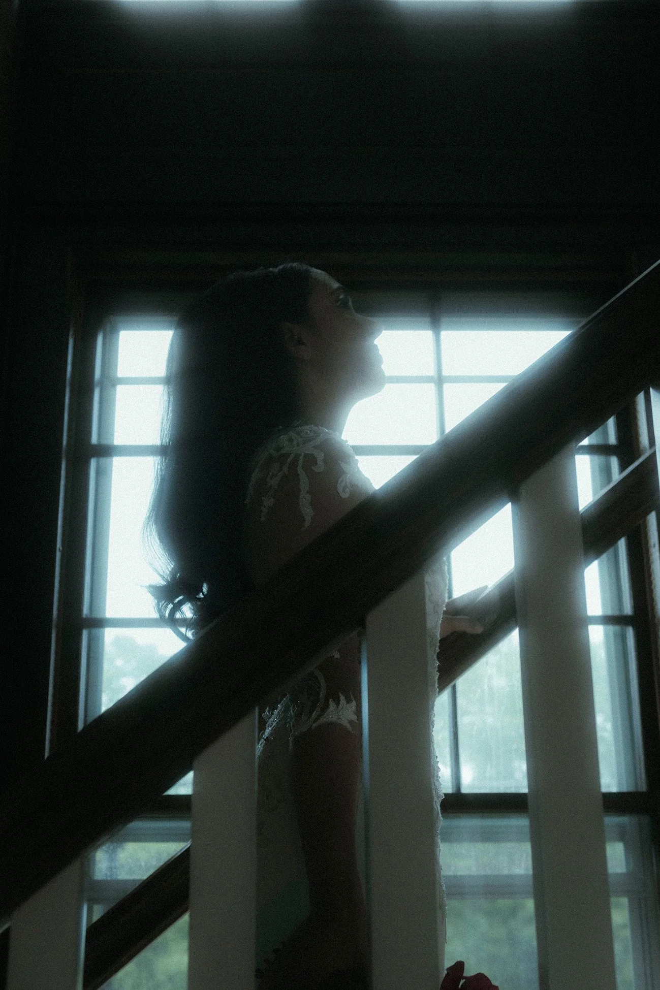 Silhouette of a woman standing by a staircase in front of a window with daylight coming through.