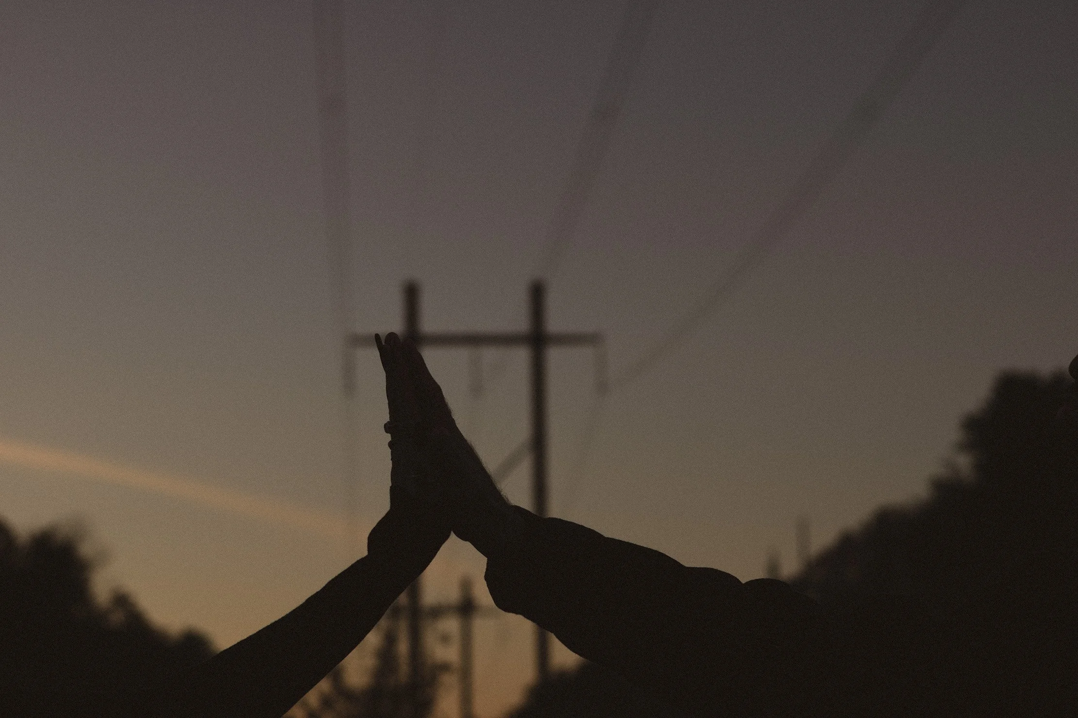 Two silhouetted people in a high five against a sunset over power lines and trees.