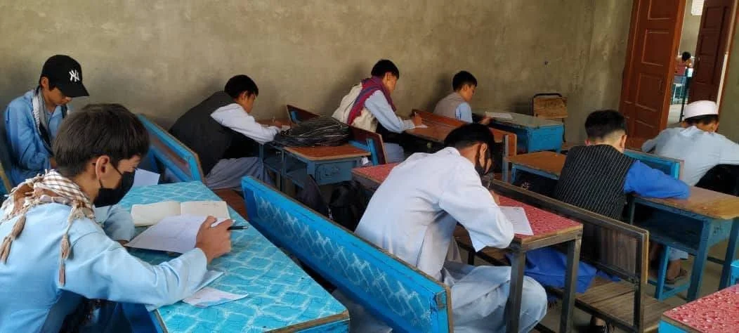 Students sitting at desks in a classroom, wearing masks and focused on their papers.