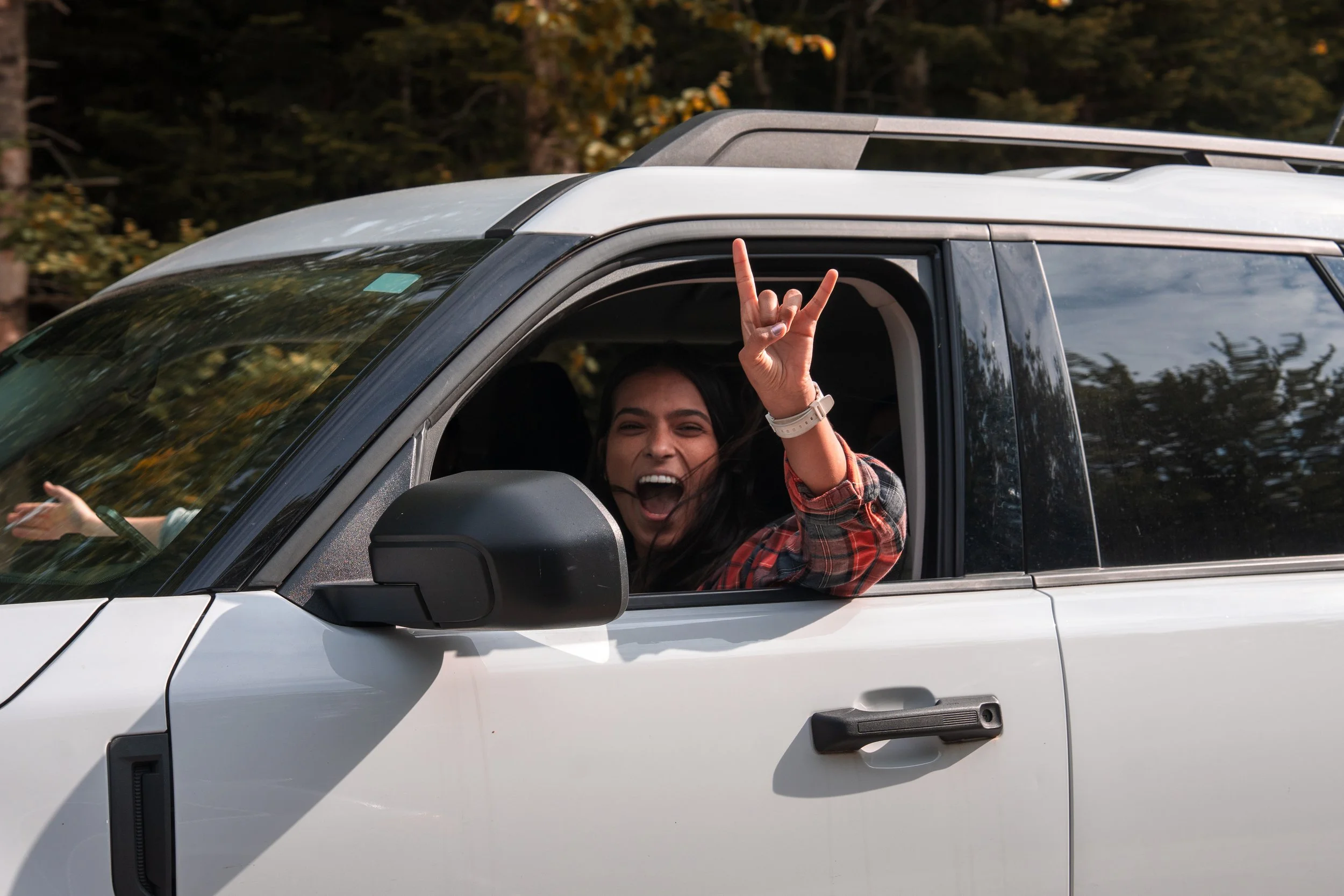 Woman smiling and making the rock on gesture through the car window during daytime.