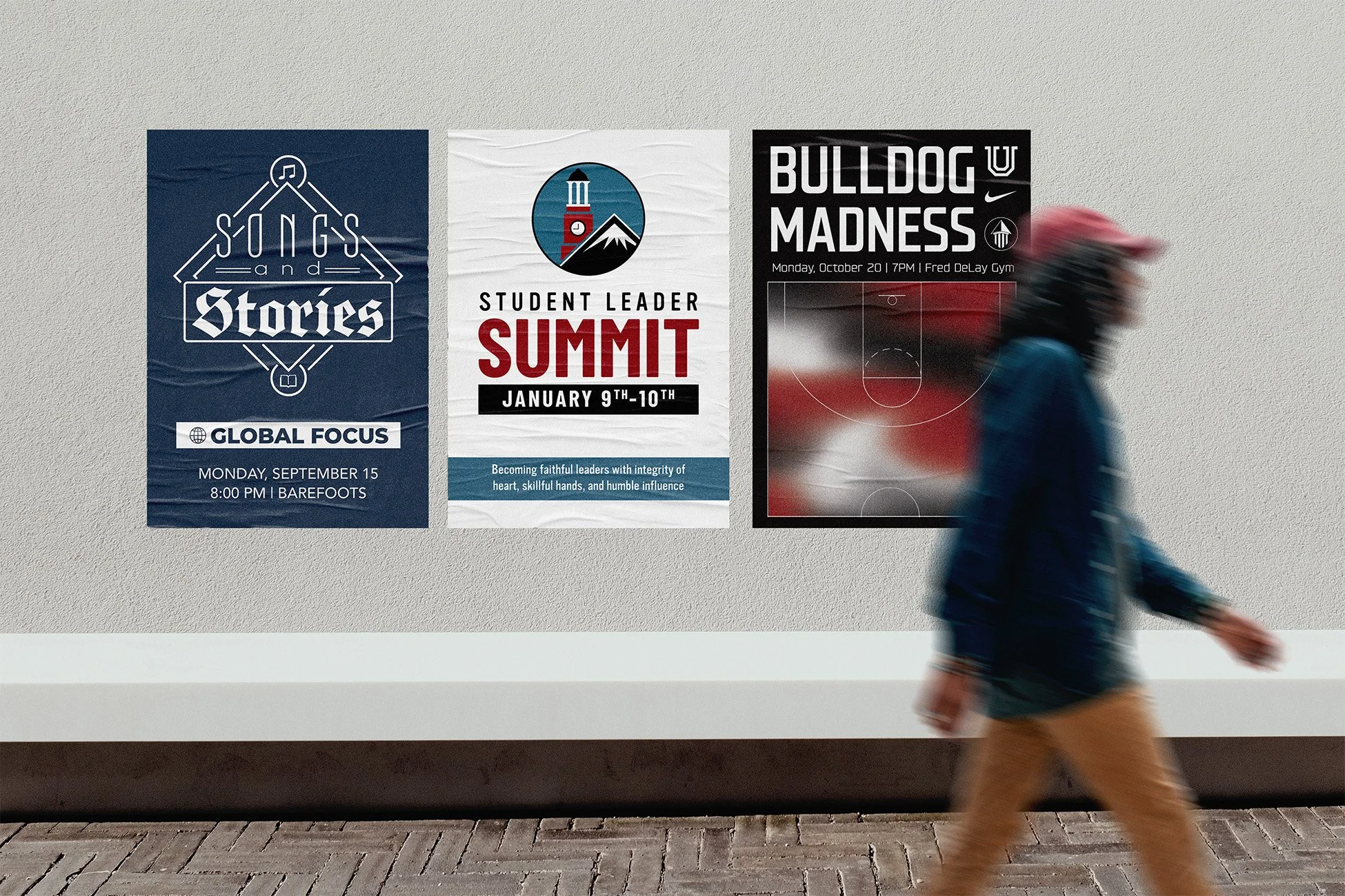 Three posters on a wall advertising a song and stories event, a student leader summit, and a basketball game, with a person walking past in the foreground.