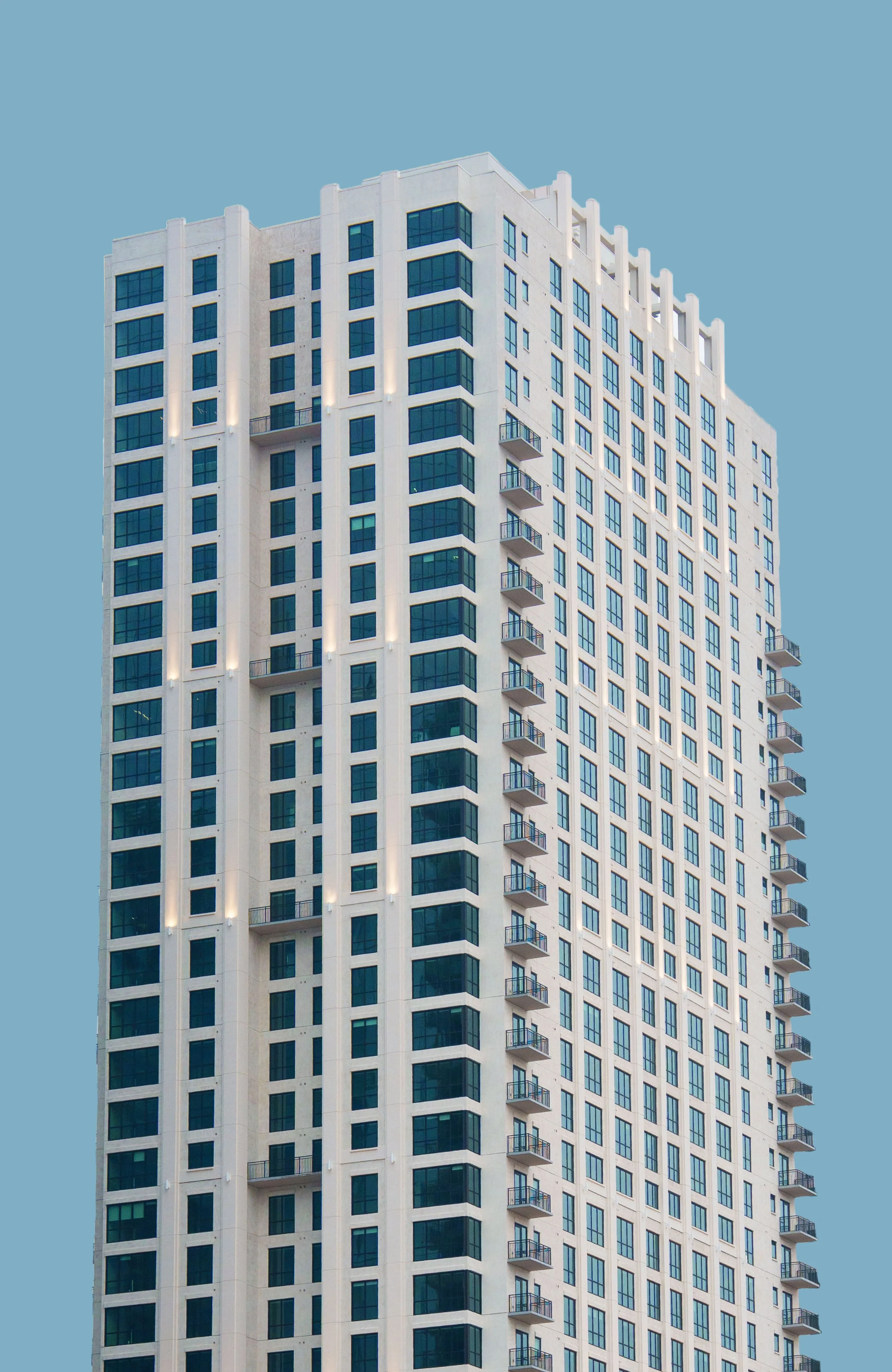 A tall modern building with white exterior and blue-tinted windows against a cloudy sky.