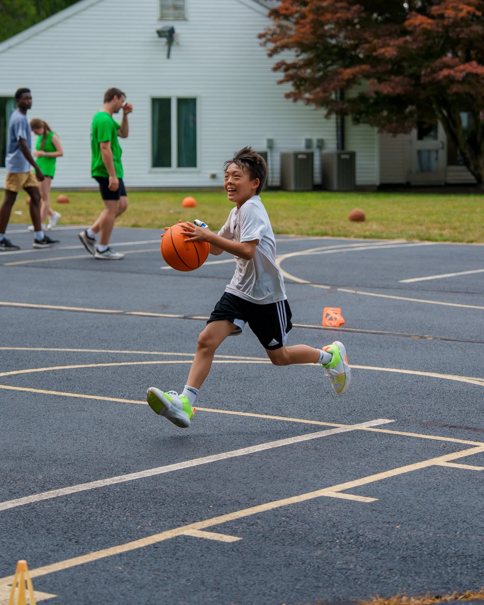 Child joyfully running with a basketball on an outdoor basketball court, with other children in the background.