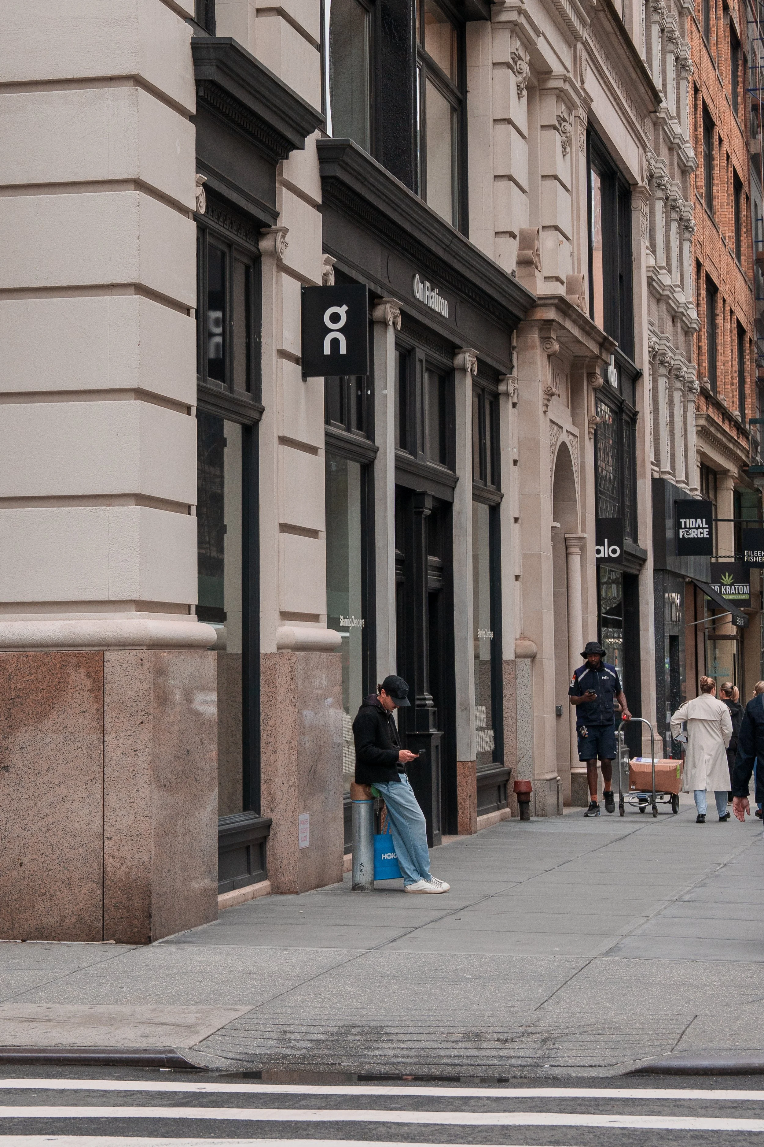 Street scene with people walking and standing outside buildings on a city sidewalk.