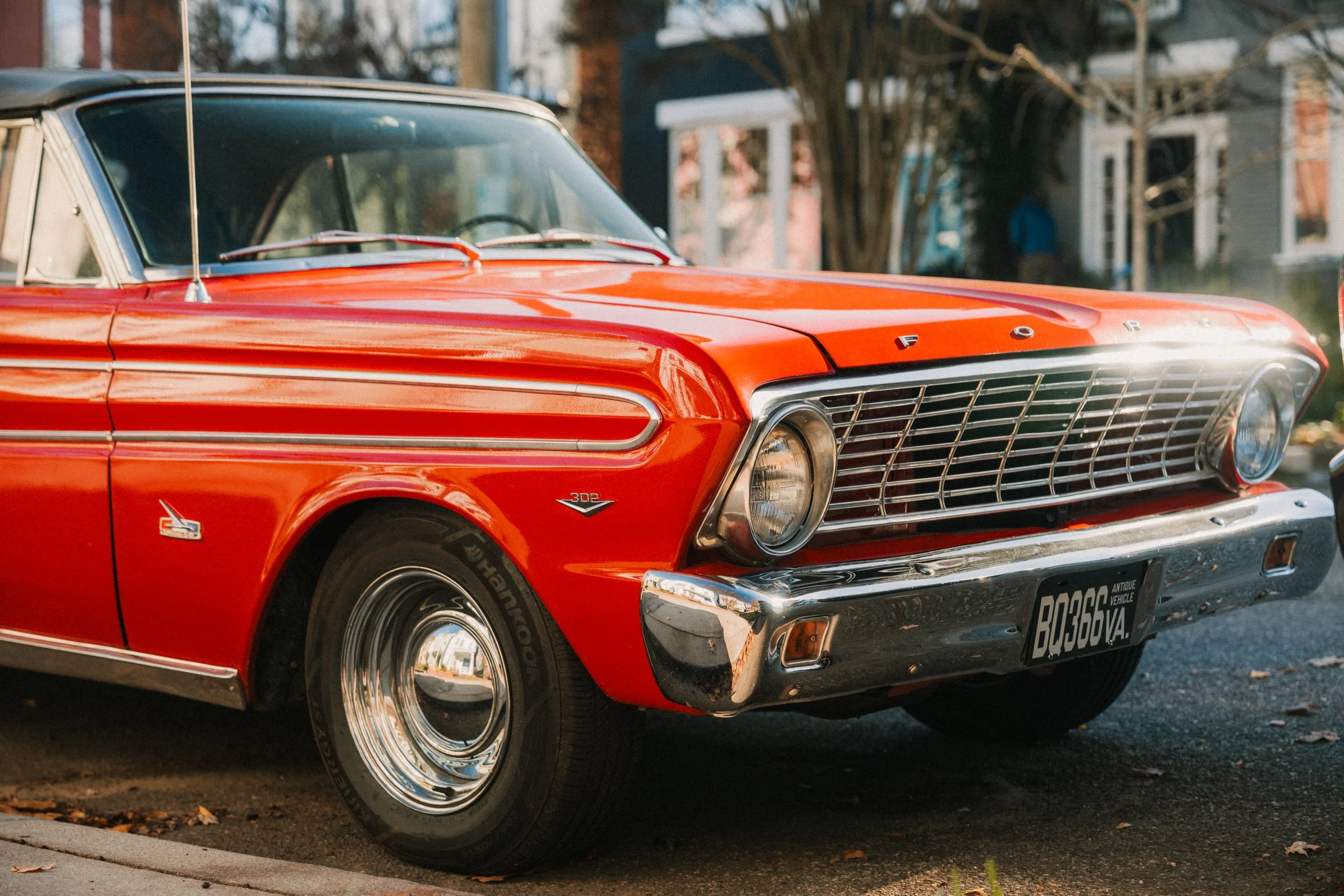 A vintage red Ford car parked on a residential street with trees and houses in the background.