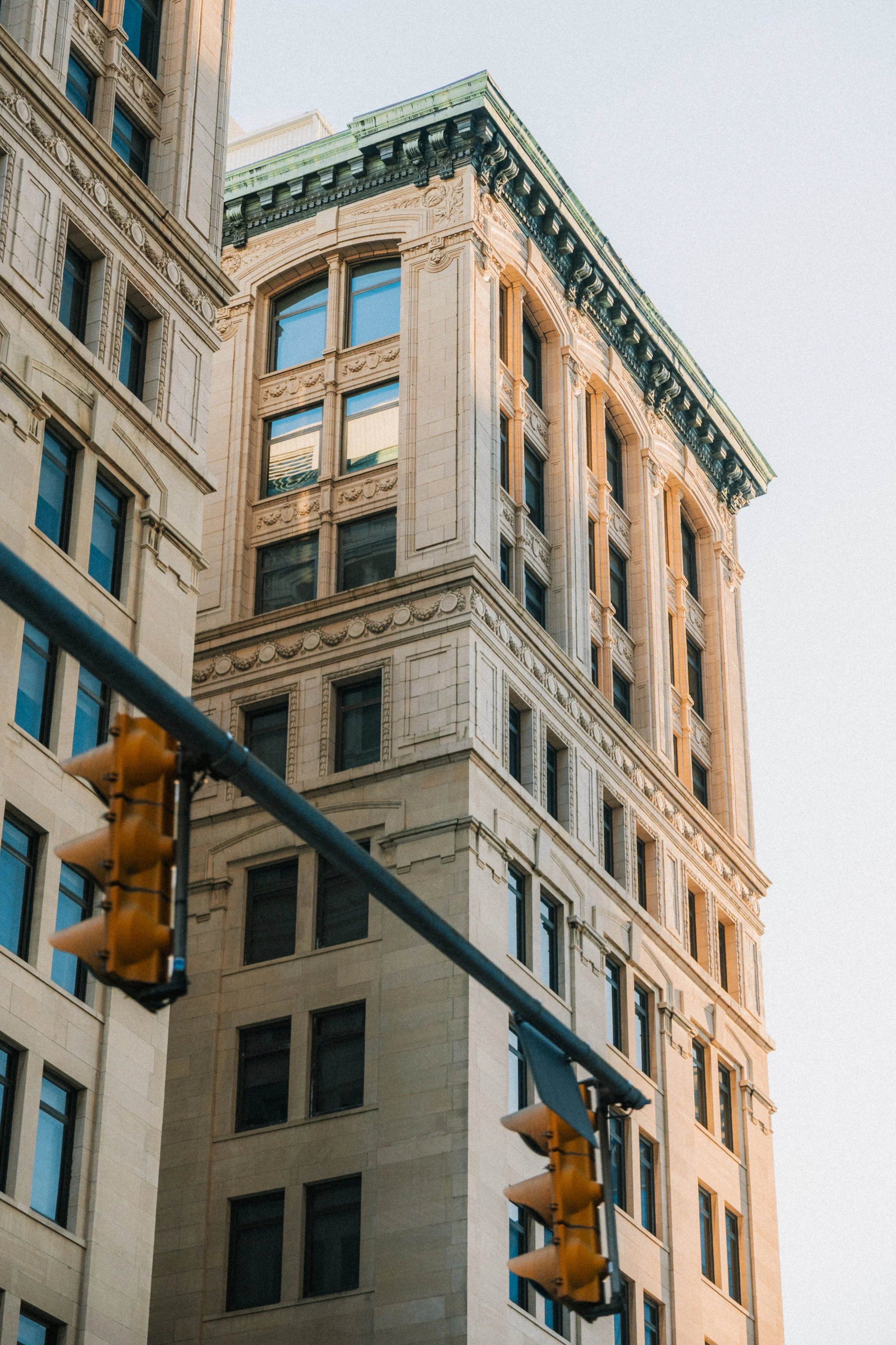 Photo of a beige historic building with detailed architectural features, standing behind traffic lights at an urban intersection.