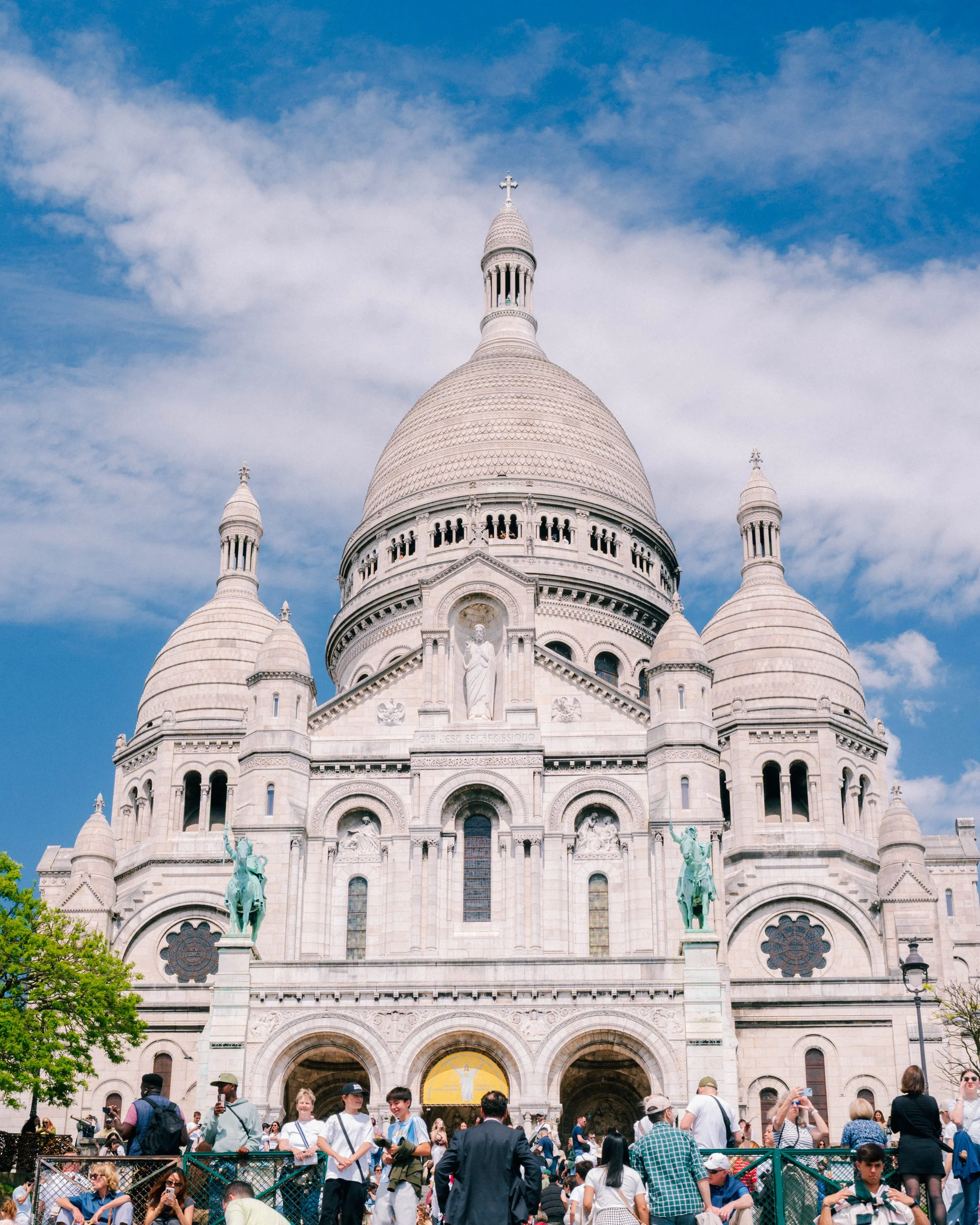 View of the Basilica of the Sacré-Cœur in Paris, France, with a crowd of tourists and visitors in the foreground.