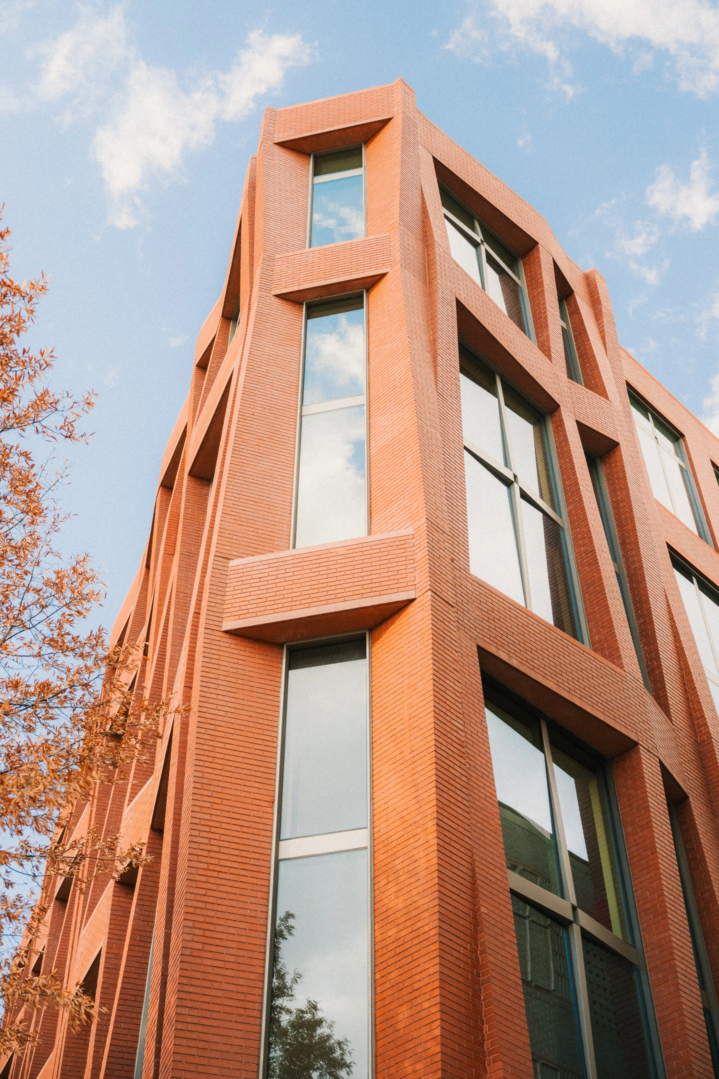 A modern brick apartment building with large reflective windows, captured from a low angle with a blue sky and clouds in the background.