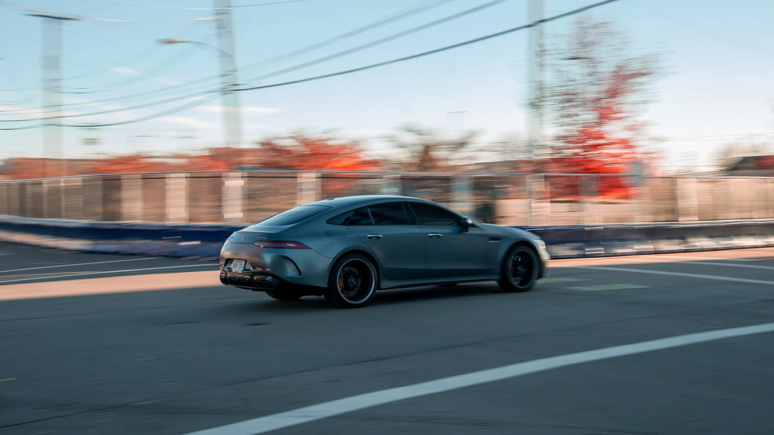 A sleek gray sedan driving on a highway with a blurred background of trees and utility poles, indicating motion.