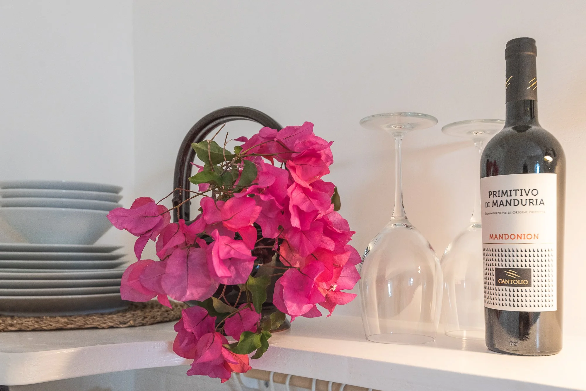 Bunte Bougainvillea-Blumen, leere Weingläser und eine Weinflasche auf einem weißen Regal