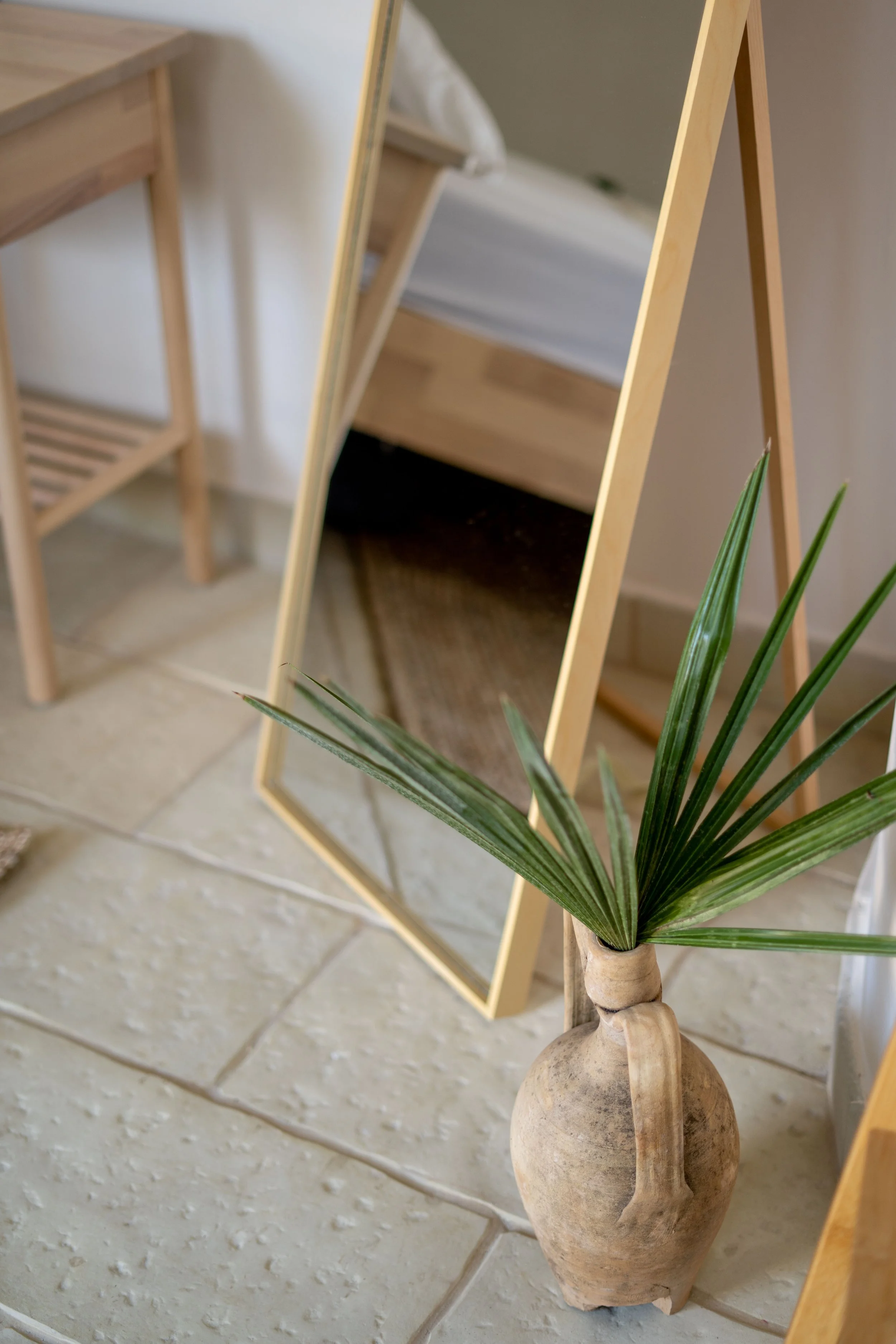 Innenaufnahme eines Raumes mit einem Vollspiegel, einer Pflanze in einem Tontopf und Holzmöbeln.