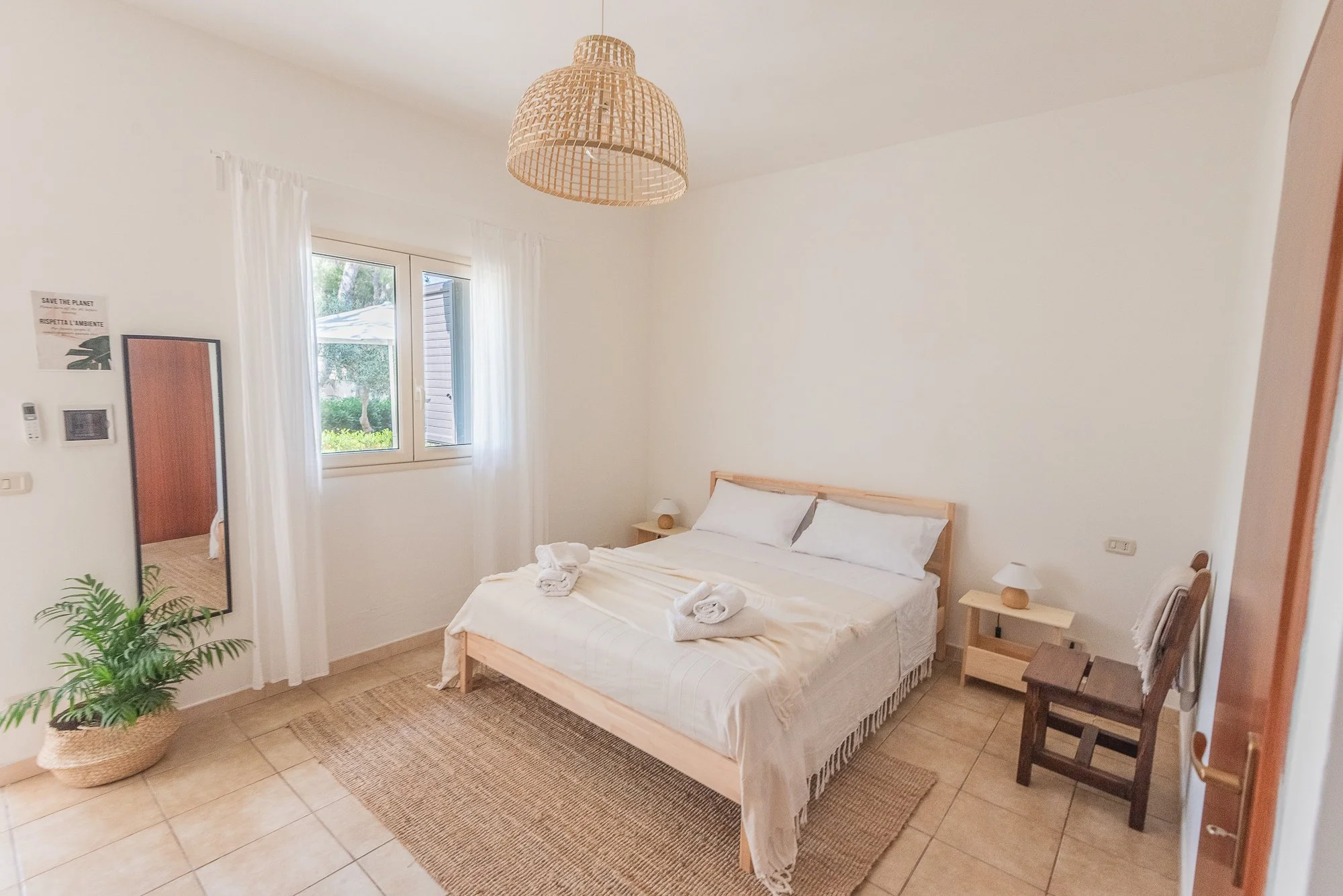 Schlafzimmer mit weißem Bett, Fenster, Pflanzen und minimalistischem Dekor im Naturstil.