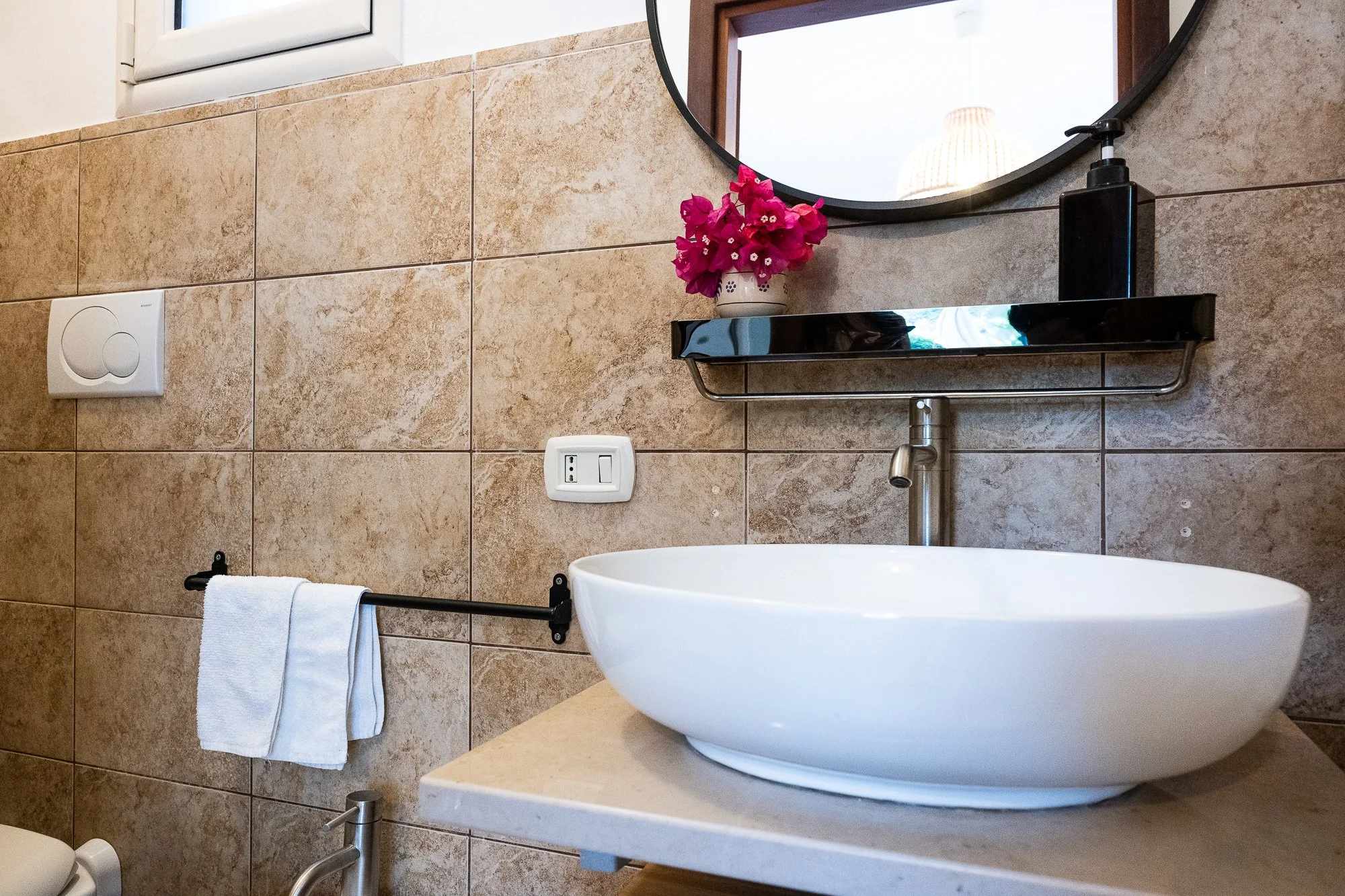Waschbecken mit Spiegel, Blumentopf mit pinken Blumen, Handtuchhalter mit weißem Handtuch, Steinplatte