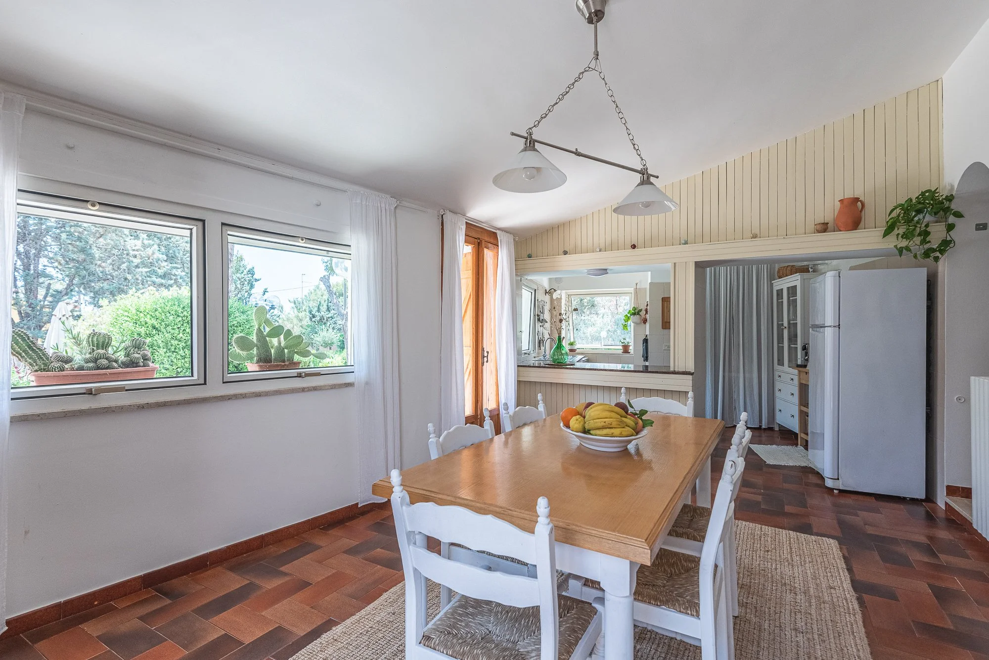 Kühlschrank im Esszimmer, Blick in die Küche, Holztisch mit Obst, Fenster mit Pflanzen, weiße Stühle, rustikaler Stil