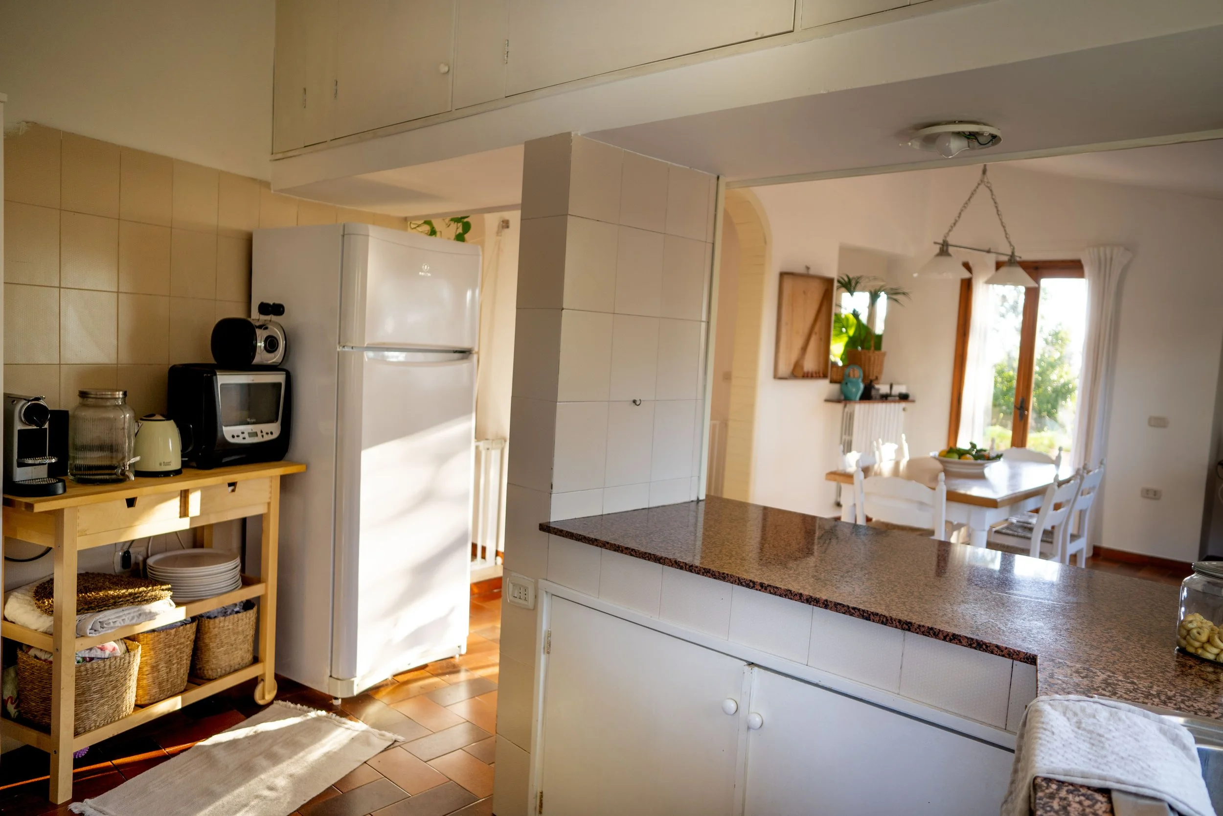 Küche mit weißen Schränken, Marmorarbeitsplatte und Essbereich mit Tisch und Stühlen vor großen Fenstern.