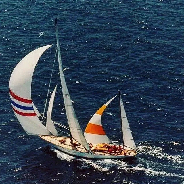 A sailboat with multiple sails, including a colorful spinnaker, sailing on the ocean.