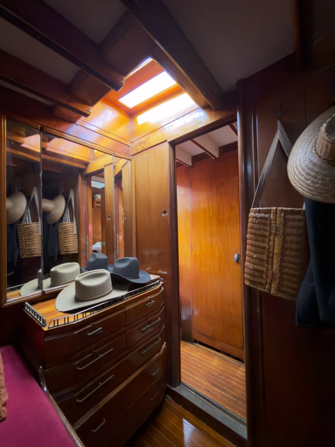 Wood-paneled closet with mirrored doors, a skylight, and hats on a dresser.