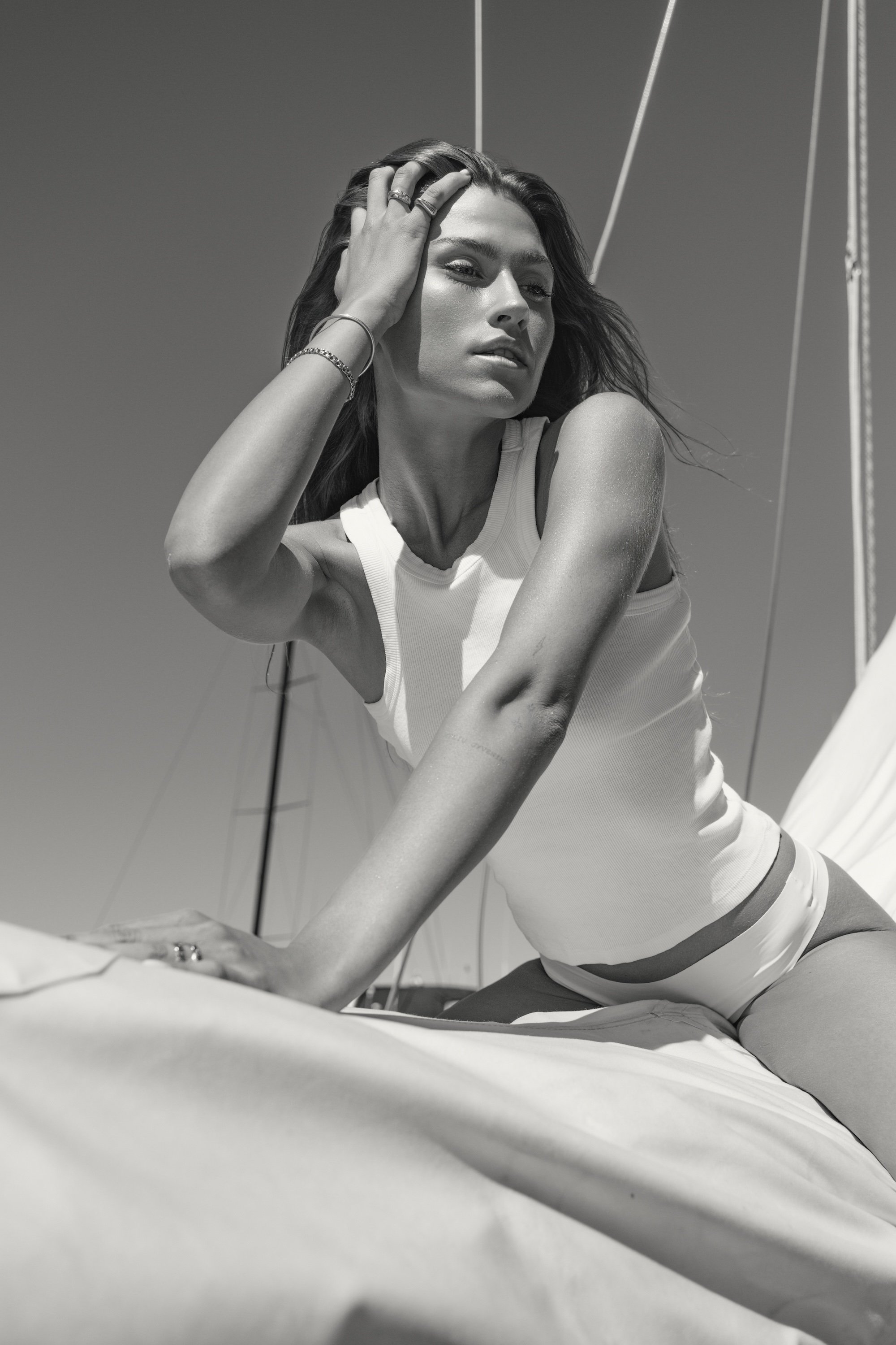 Black and white photo of a woman on a boat, posing with her hand on her head, wearing a sleeveless top and shorts.