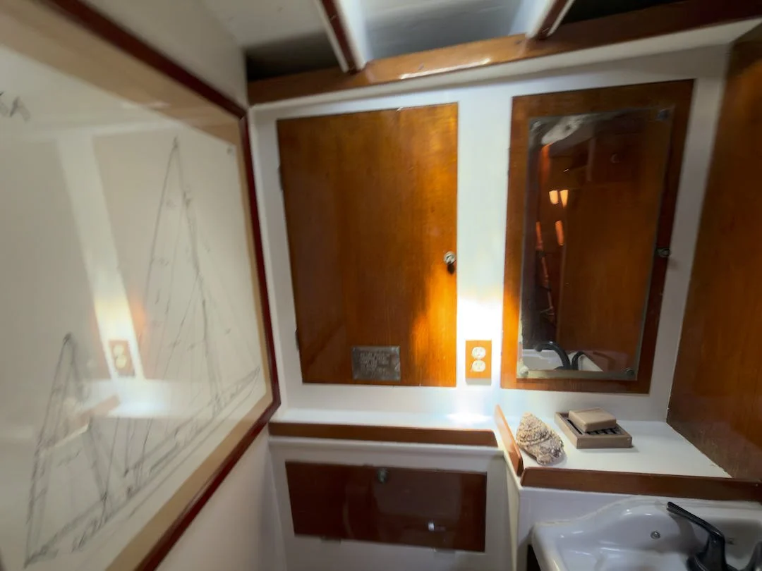 A room with a wooden cabinet, a mirror, a sink, and framed sketches of sailboats on the wall.