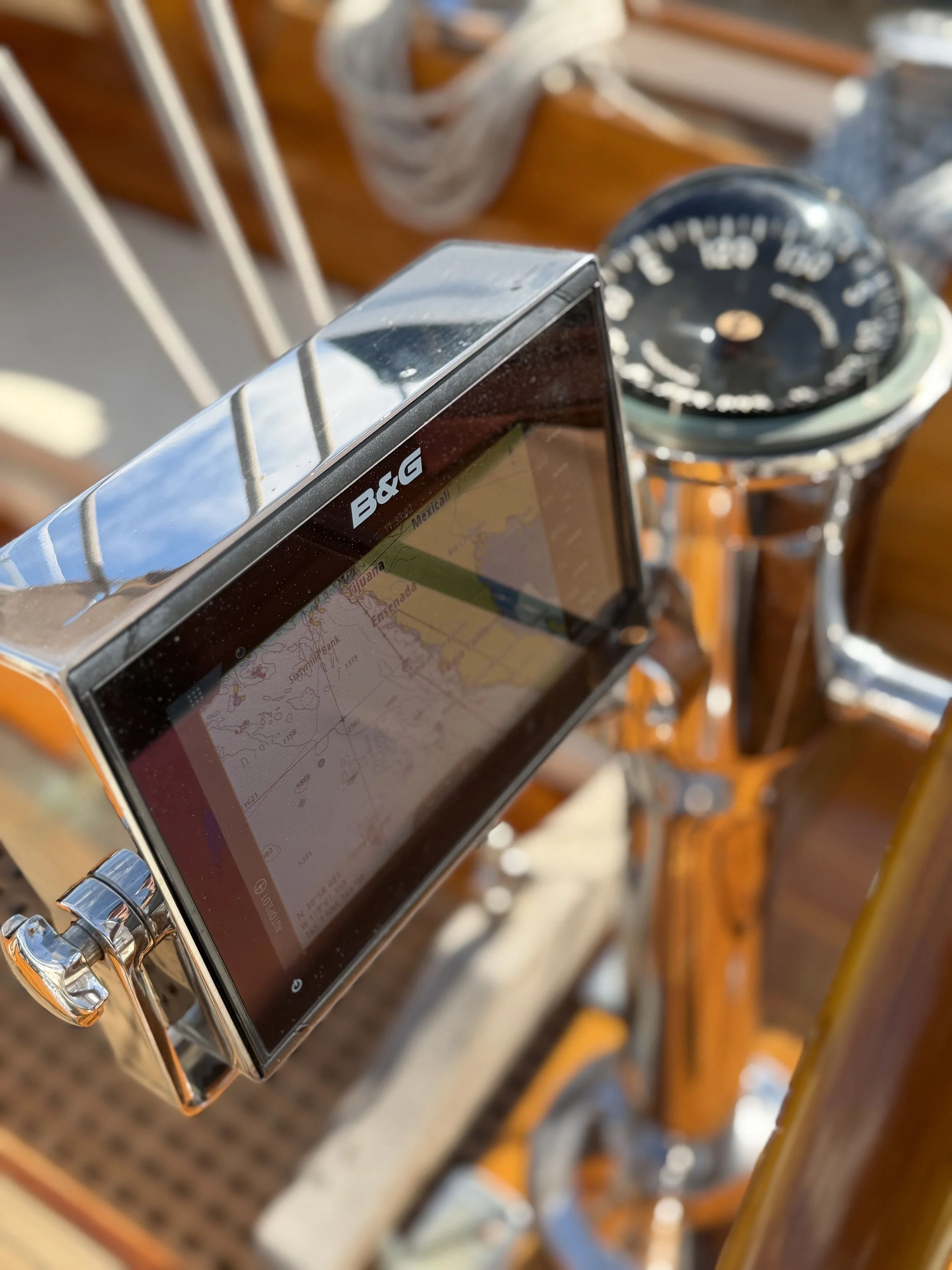 A GPS device mounted on the handlebar of an orange bicycle, with a compass in the background. The GPS screen shows a map during daylight.
