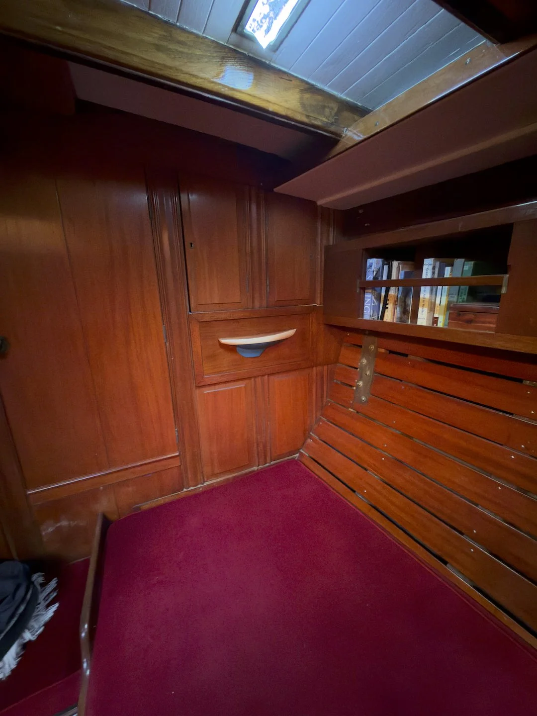 Wood-paneled interior with a built-in bookcase holding books and a red carpeted seating area with a wooden bench.