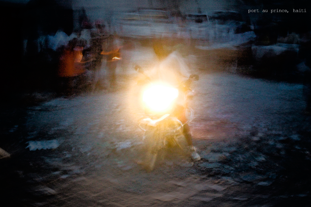 A person on a boat holding a glowing light, with other boats in the background on the water at Port-au-Prince, Haiti.