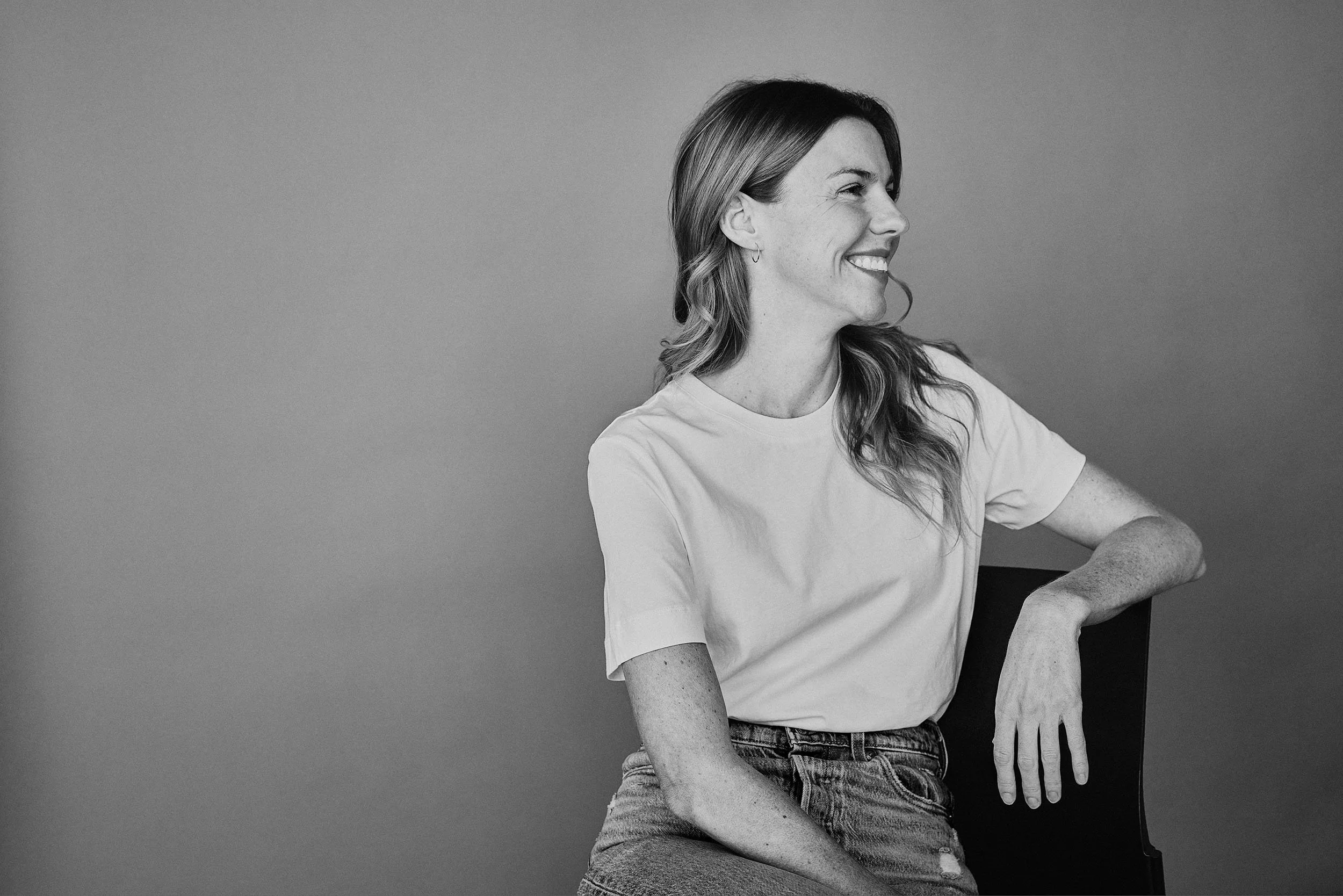 Karina Durand souriante assise sur une chaise contre un fond gris.