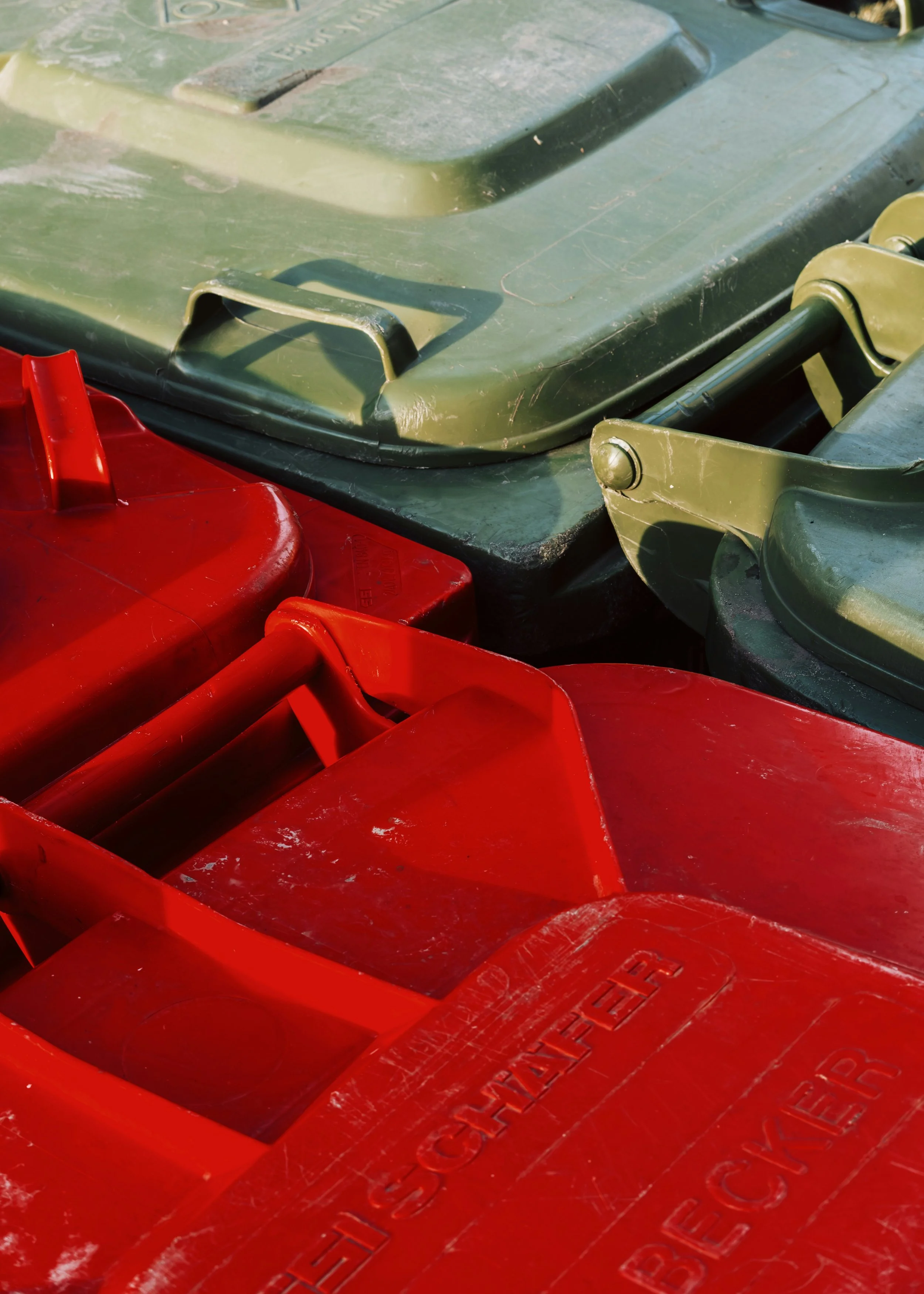 Close-up photograph of several trash cans, with two red and one green, stacked together outdoors. The cans show signs of wear and scratches.