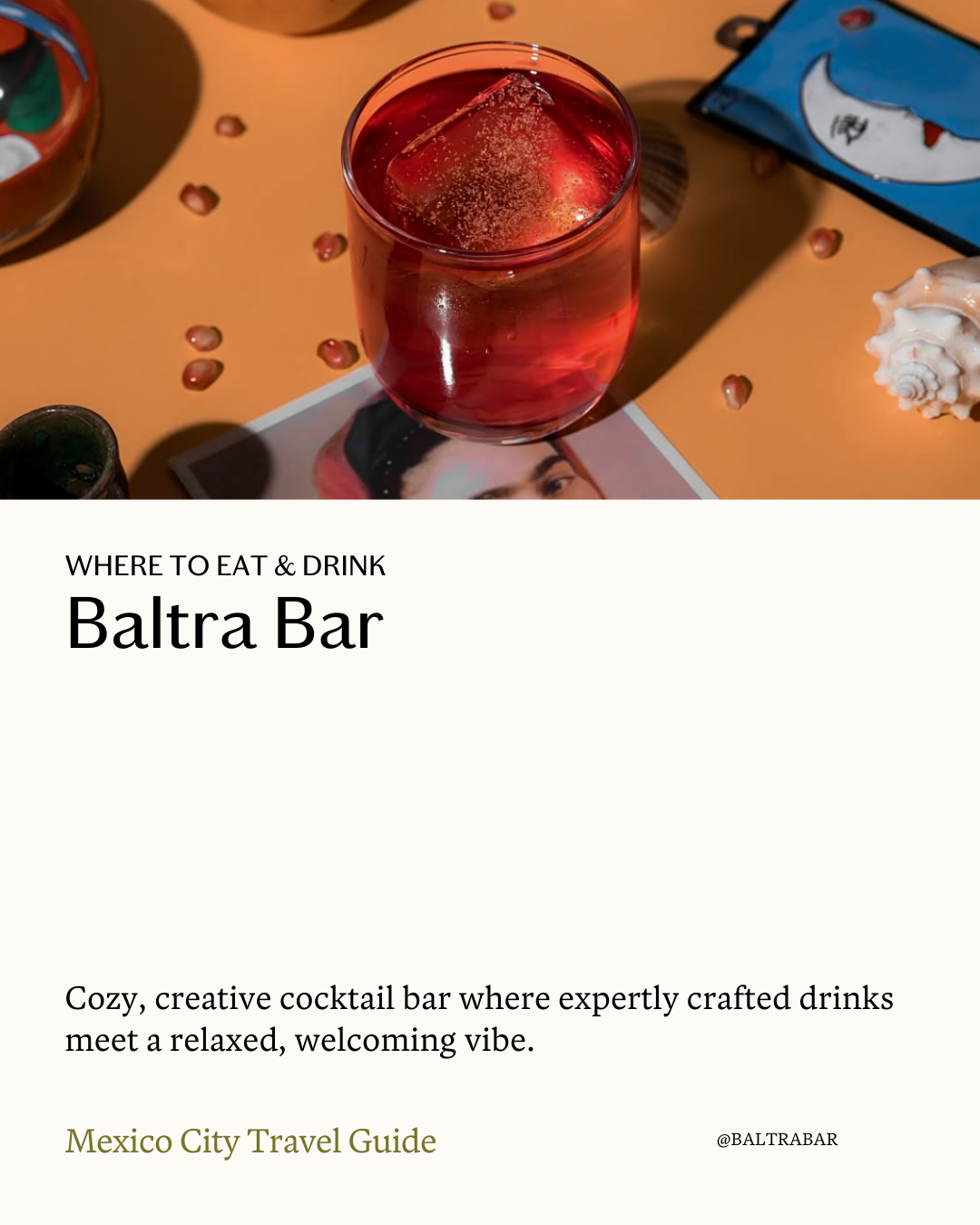 A glass of red cocktail with ice on a colorful table decorated with small beads, a book or magazine, and seashells, promoting Baltra Bar in Mexico City as a cozy, creative cocktail bar with expertly crafted drinks.