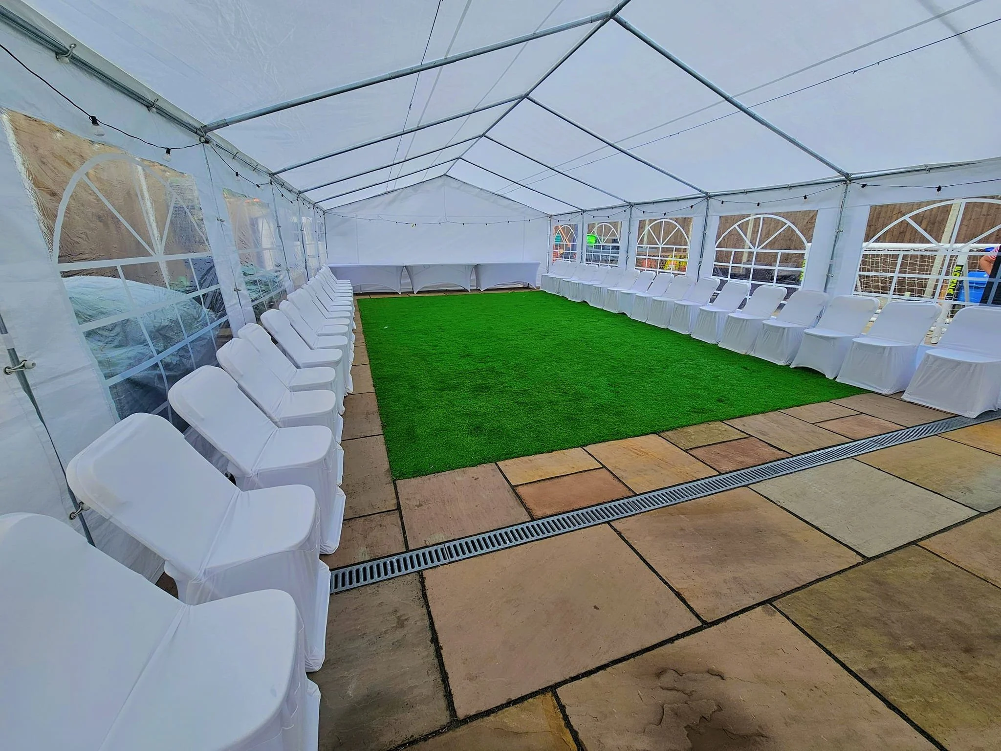 White event marquee with artificial grass flooring and banquet seating set up for a wedding or private event by NKMarquees